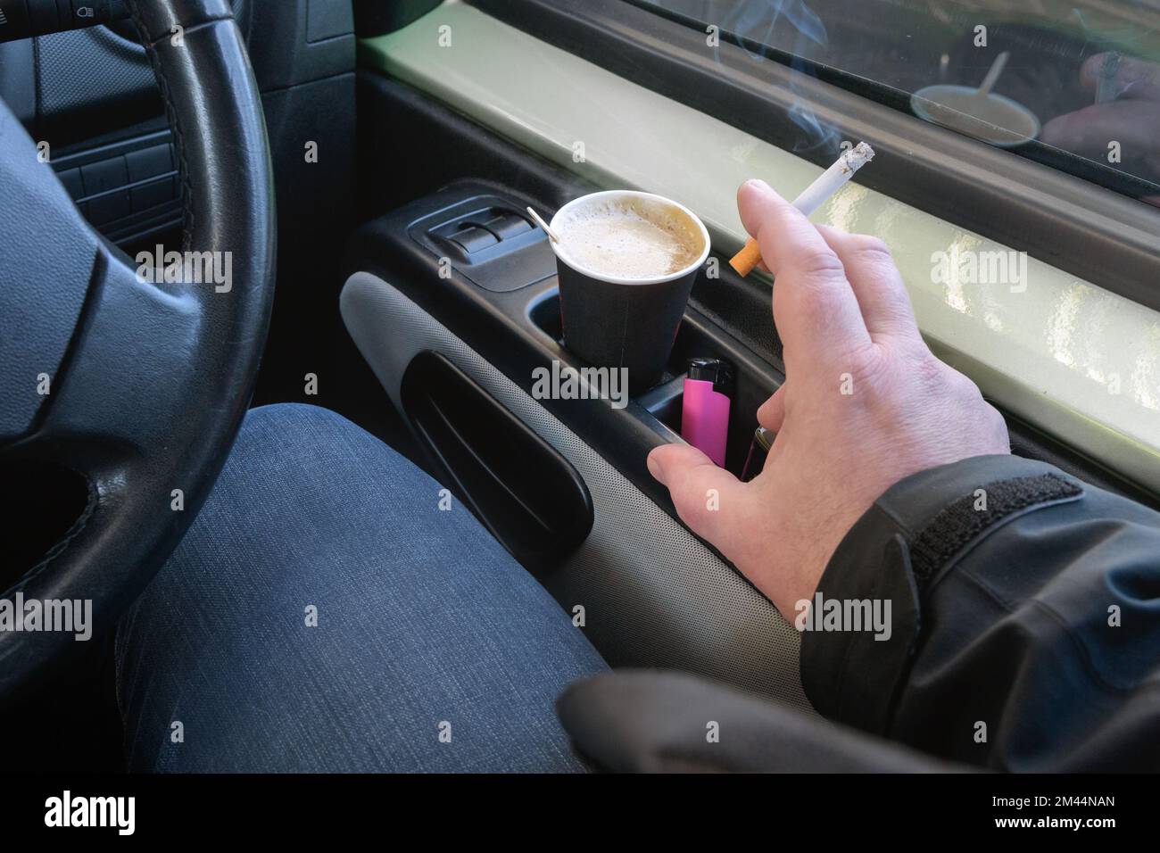 Rauchen beim Autofahren. Fahrzeug mit Rechtslenkung. Die Zigarette in der Hand. Pappkaffeetassen. Stockfoto