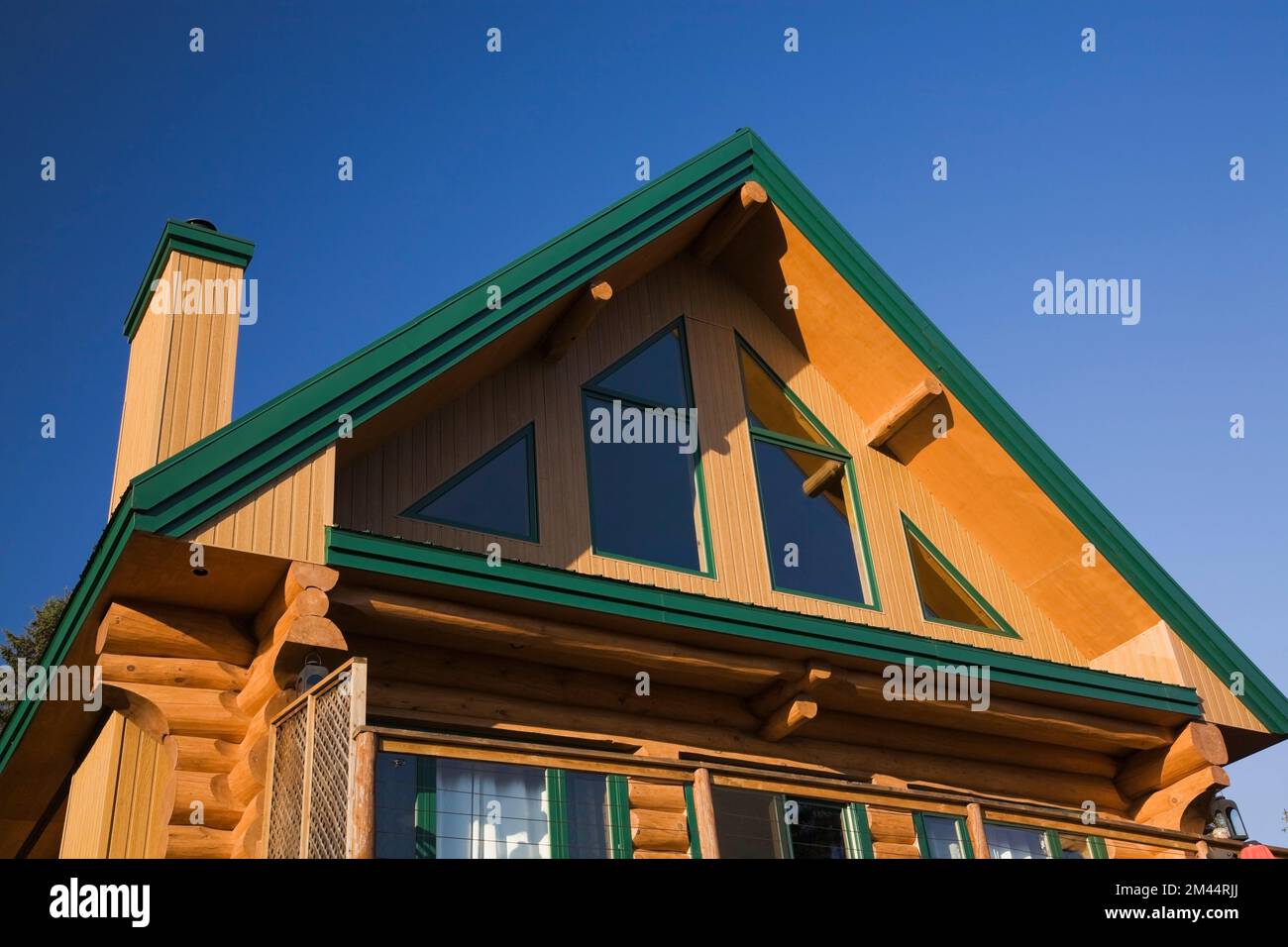 Rückansicht eines zweistöckigen Blockhauses im A-Rahmen-Stil mit Panoramafenstern und grüner Verkleidung im Herbst. Stockfoto