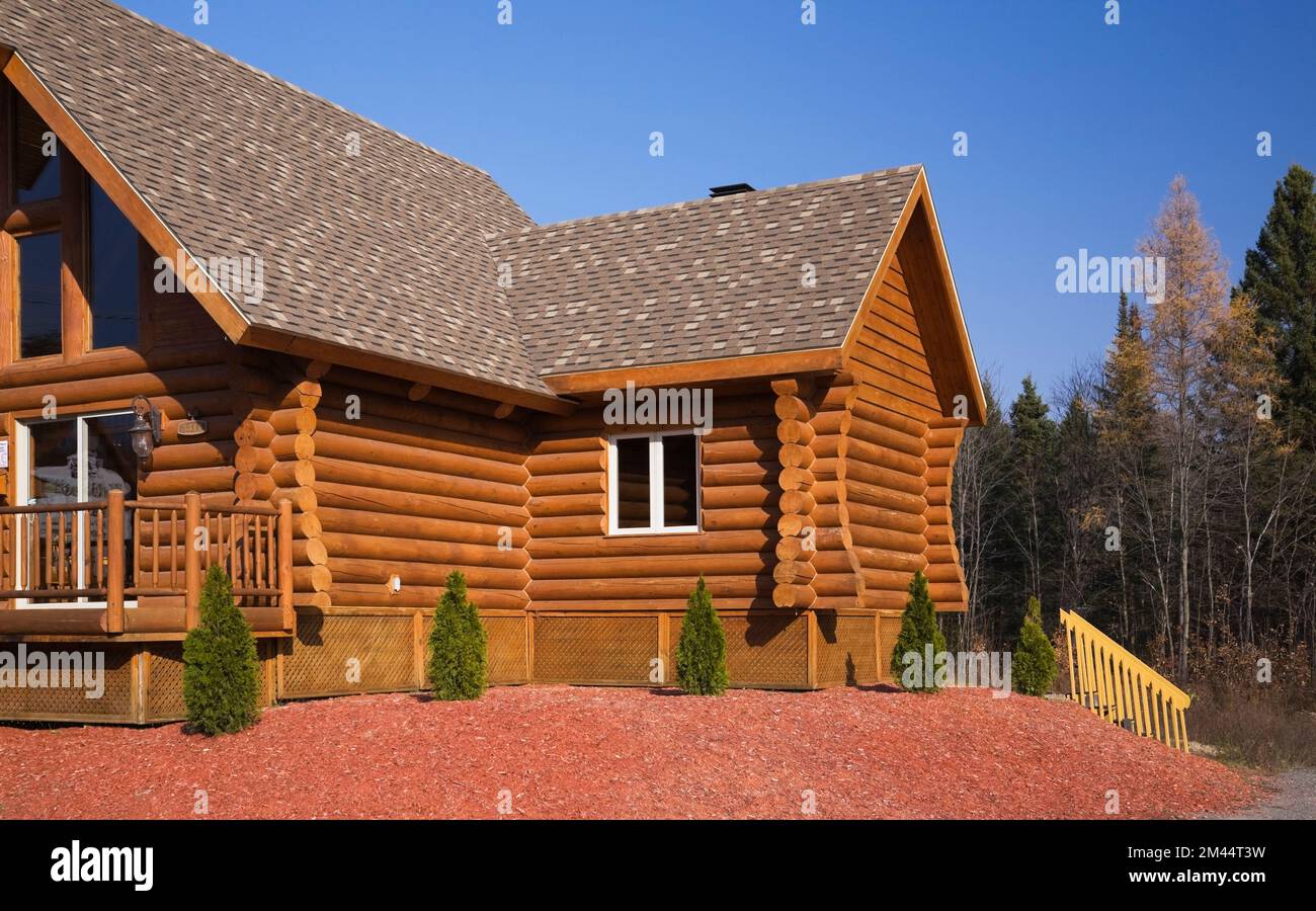 Braunes, rötlich gefärbtes Blockhaus mit braunem und braunem Asphaltschindeldach im Herbst. Stockfoto