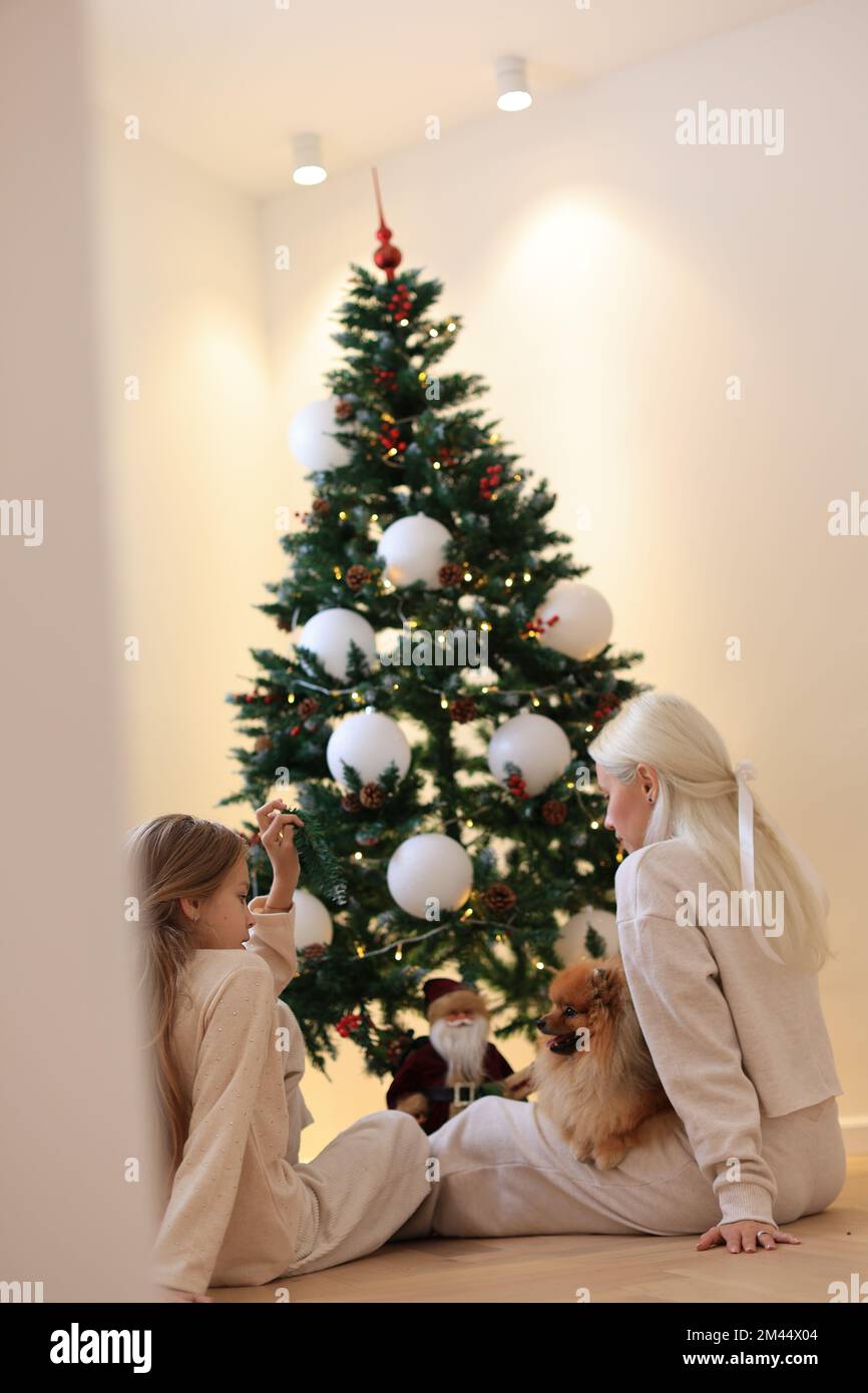 Frohe Weihnachten und frohe Feiertage. Mama und Tochter schmücken den Weihnachtsbaum im Zimmer. Liebende Familie drinnen Stockfoto