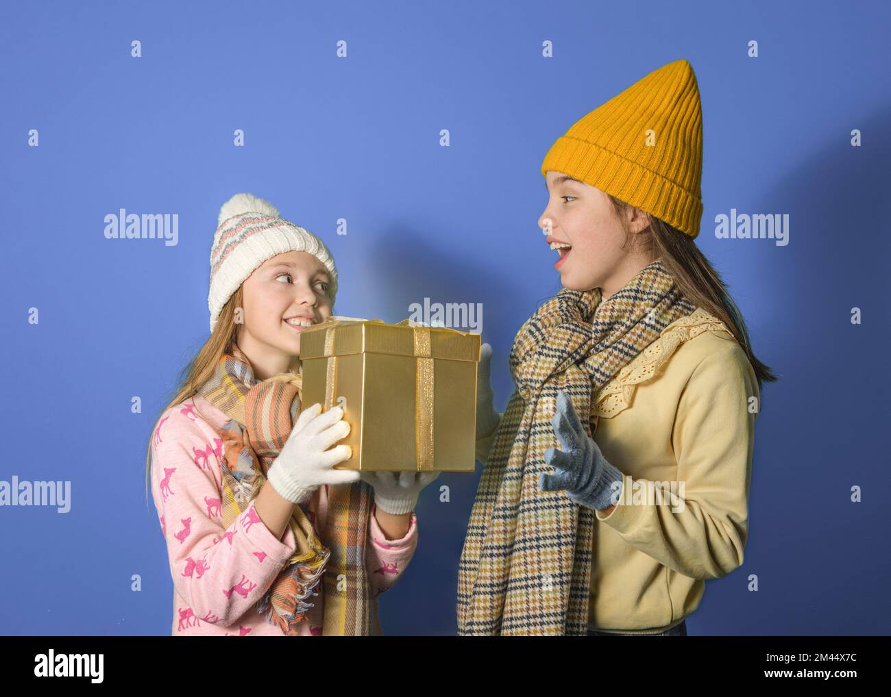 Das Mädchen schenkt ihrer älteren Schwester ein Geschenk. Familientraditionen. Zwei Teenager-Mädchen mit einem Geschenk auf blauem Hintergrund Stockfoto