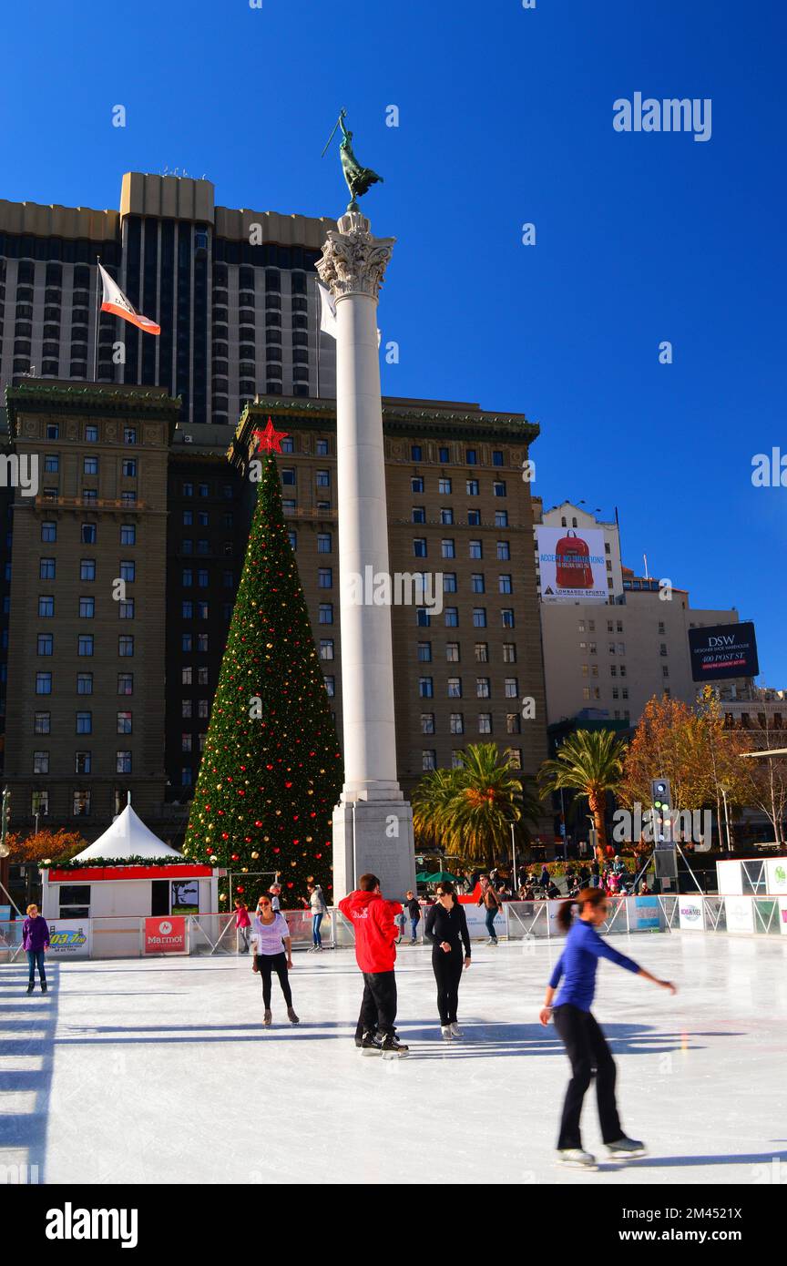 Eine kleine Gruppe von Menschen Schlittschuhlaufen an einem Wintertag vor einer großen Säule und einem Weihnachtsbaum am Union Square in San Francisco Stockfoto