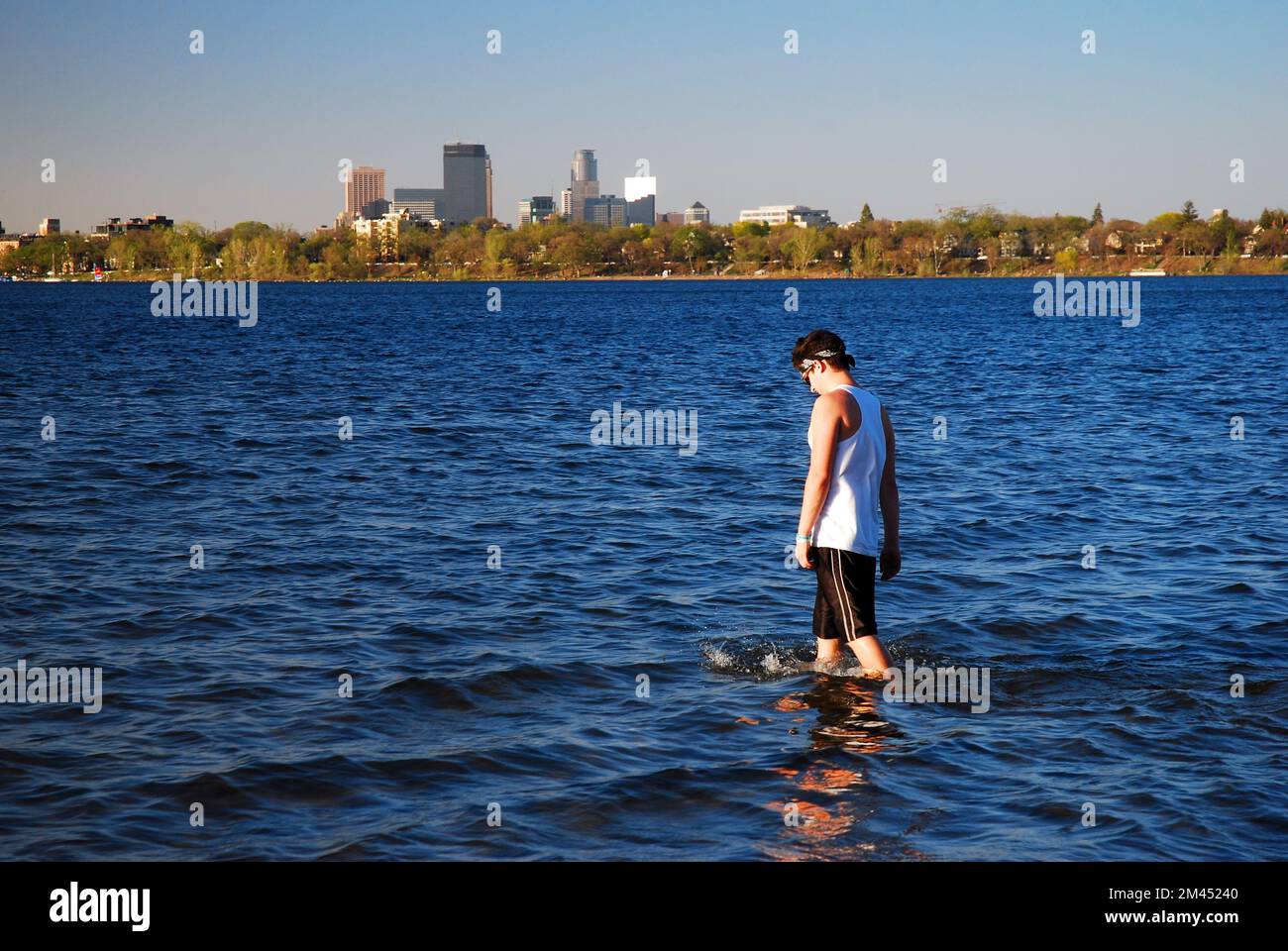 Ein erwachsener Mann waten am Lake Calhoun, mit der Skyline von Minneapolis im Hintergrund, an einem sonnigen Sommerferientag Stockfoto