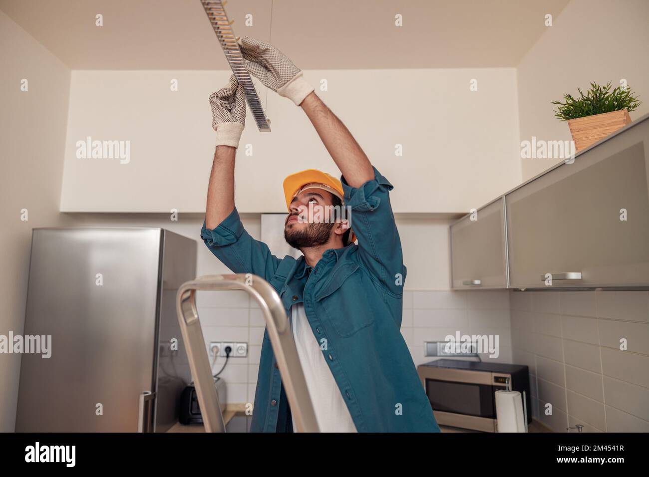 Ein professioneller Elektriker in Uniform installiert elektrische Lampen in der Küche Stockfoto