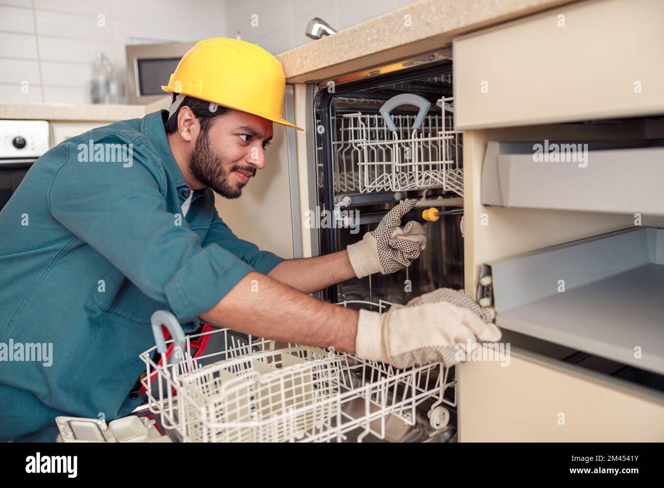 Fokussierter Handwerker in Spezialkleidung, der Geschirrspüler in der modernen Küche repariert Stockfoto