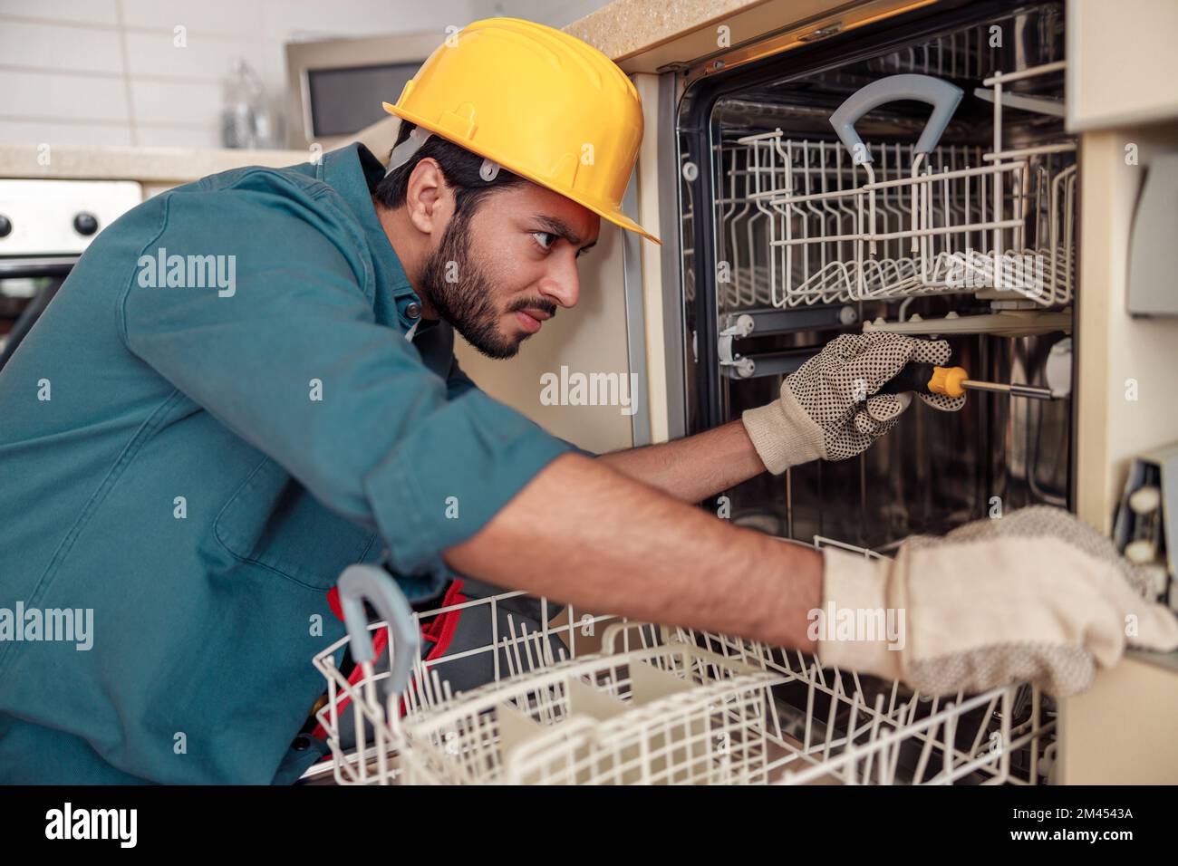 Fokussierter Handwerker in Spezialkleidung, der Geschirrspüler in der modernen Küche repariert Stockfoto