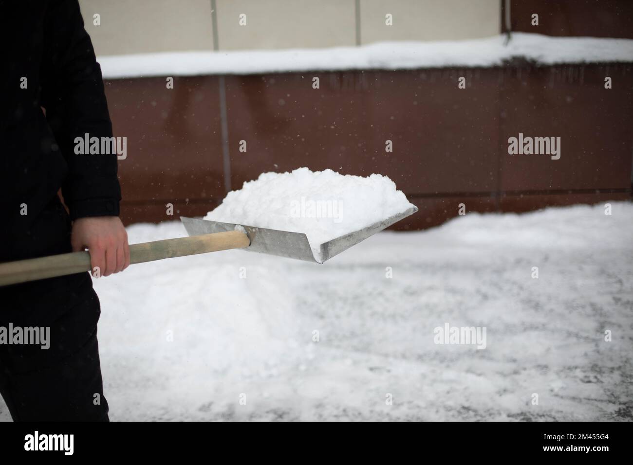 Schneeräumung auf der Straße. Schaufel für die Kettenreinigung. Der Mann räumt den Hof auf. Große Schaufel. Stockfoto
