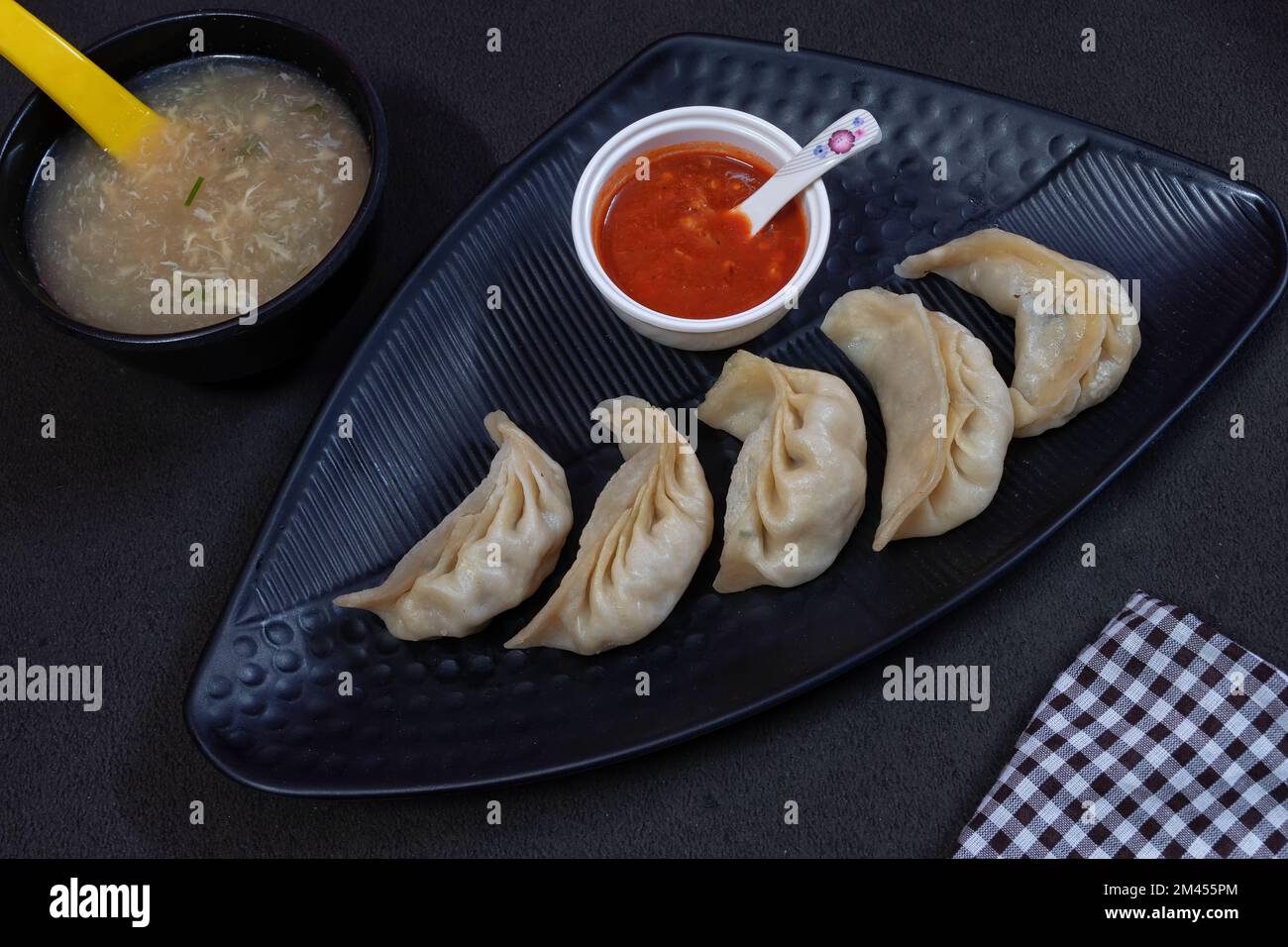 Bild von gedünstetem gefülltem momo mit Hühnchen, serviert auf einem schwarzen Teller, zusammen mit Hühnersuppe in einer Schüssel und Sauce auf schwarzem Hintergrund. Stockfoto
