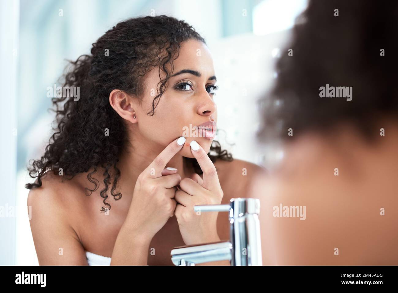 Ich brauche eine dauerhaftere Lösung. Eine schöne junge Frau, die einen Pickel drückt, während sie in den Spiegel schaut. Stockfoto