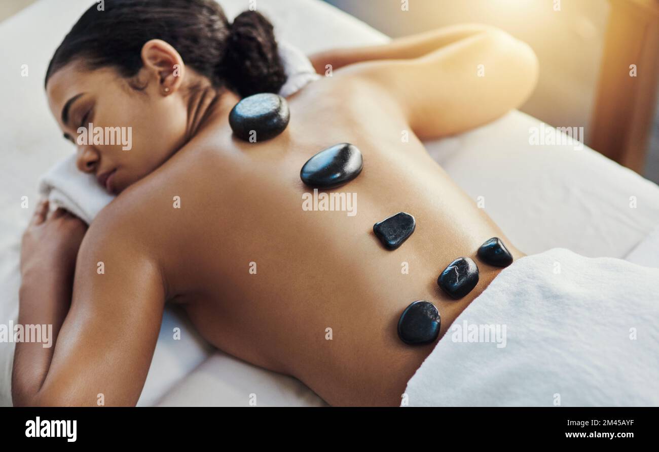 Er zielt auf schmerzende Muskeln mit etwas Hitze. Eine junge Frau, die eine Hot-Stone-Massage in einem Spa bekommt. Stockfoto