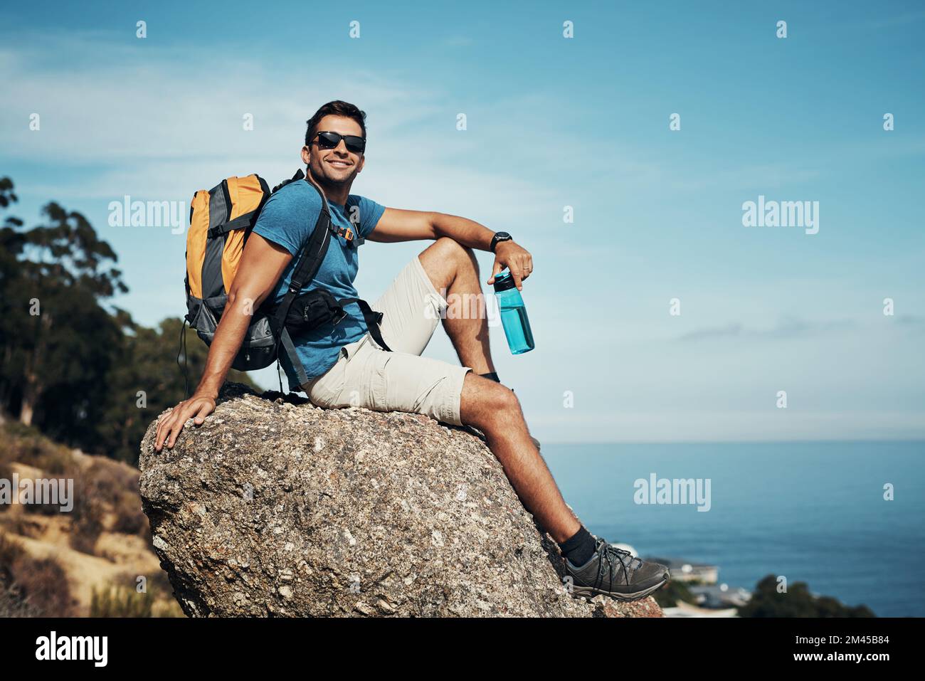 Ich hänge nur rum. Porträt eines sorglosen jungen Mannes, der tagsüber eine kurze Pause vom Wandern auf einen Berg macht. Stockfoto