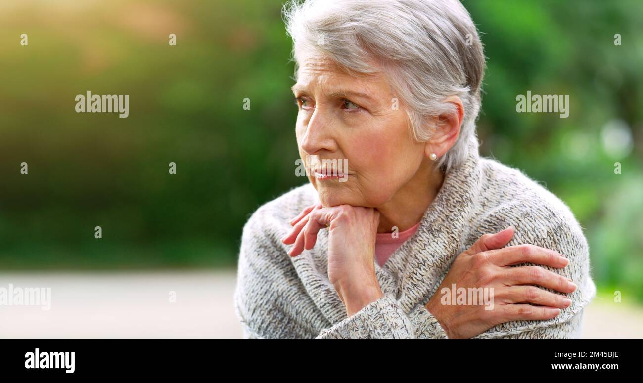 Mein Leben ist so schnell vorbei. Eine sorglose ältere Frau, die auf einer Bank sitzt, während sie im Park im Freien nachdenkt. Stockfoto