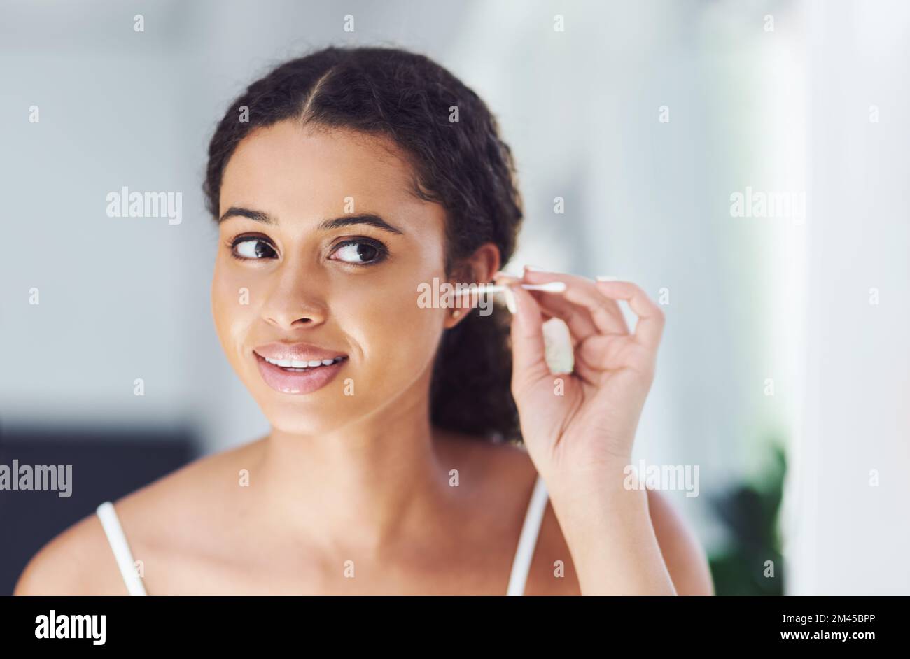 Man muss sich um die schwer erreichbaren Stellen kümmern. Eine attraktive junge Frau, die sich die Ohren mit einem Wattestäbchen putzt. Stockfoto