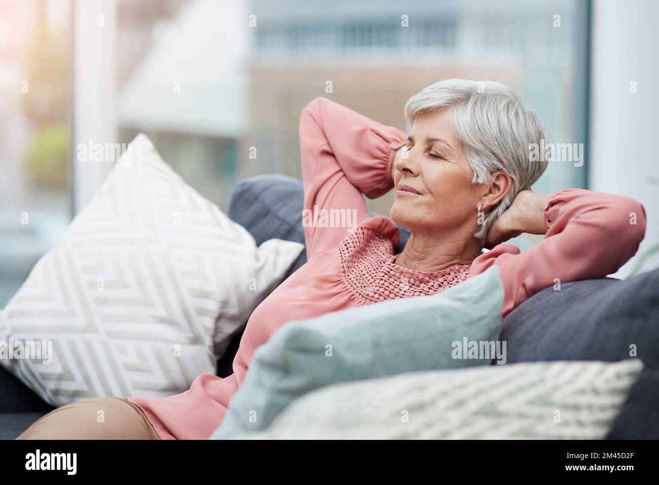 Zeit zum Entspannen. Fröhliche, reife Frau, entspannt und entspannt auf ihrem Sofa zu Hause. Stockfoto
