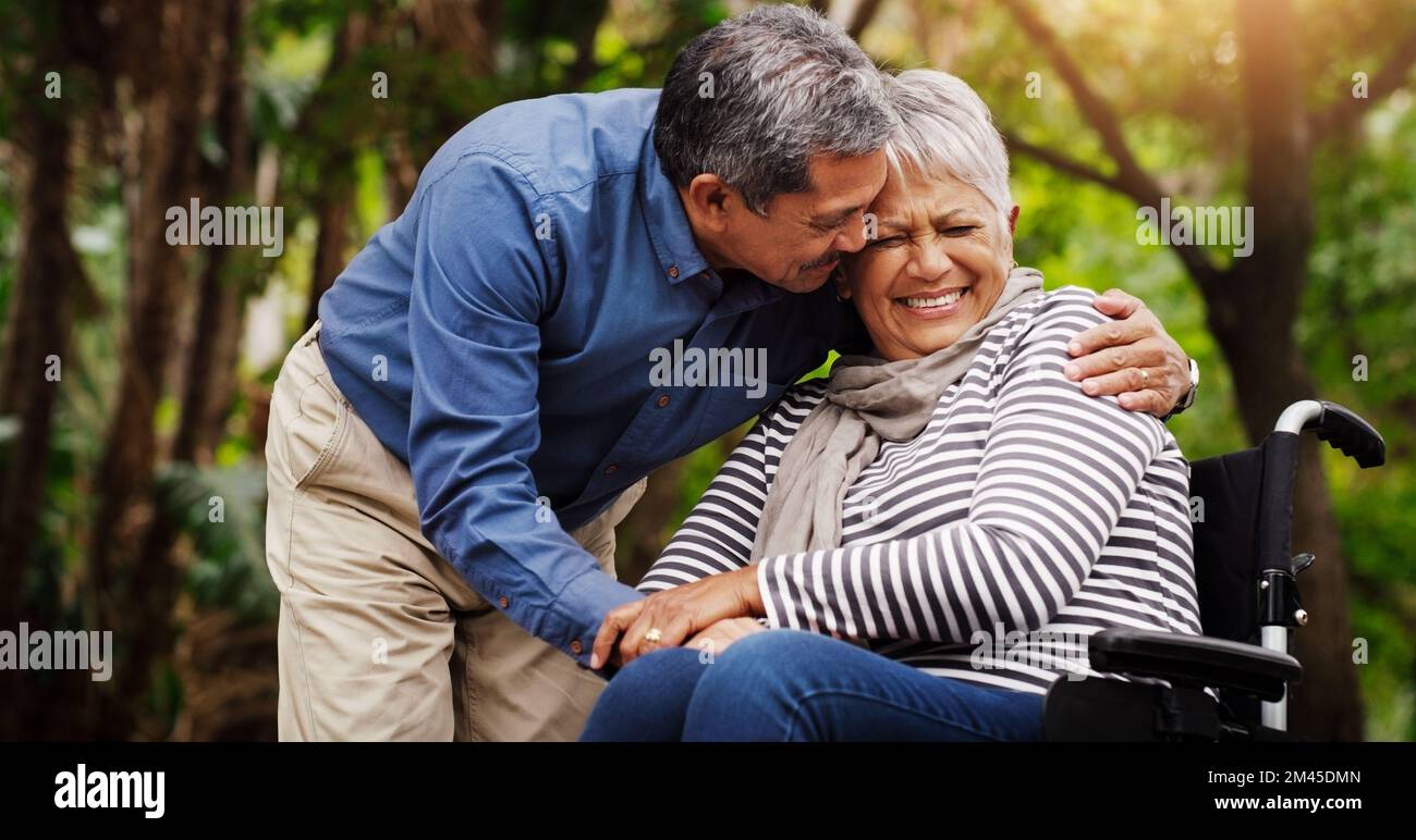 Liebe kann alles aushalten. Eine glückliche, im Rollstuhl gefesselte ältere Frau, die den Tag mit ihrem Mann im Park verbringt. Stockfoto