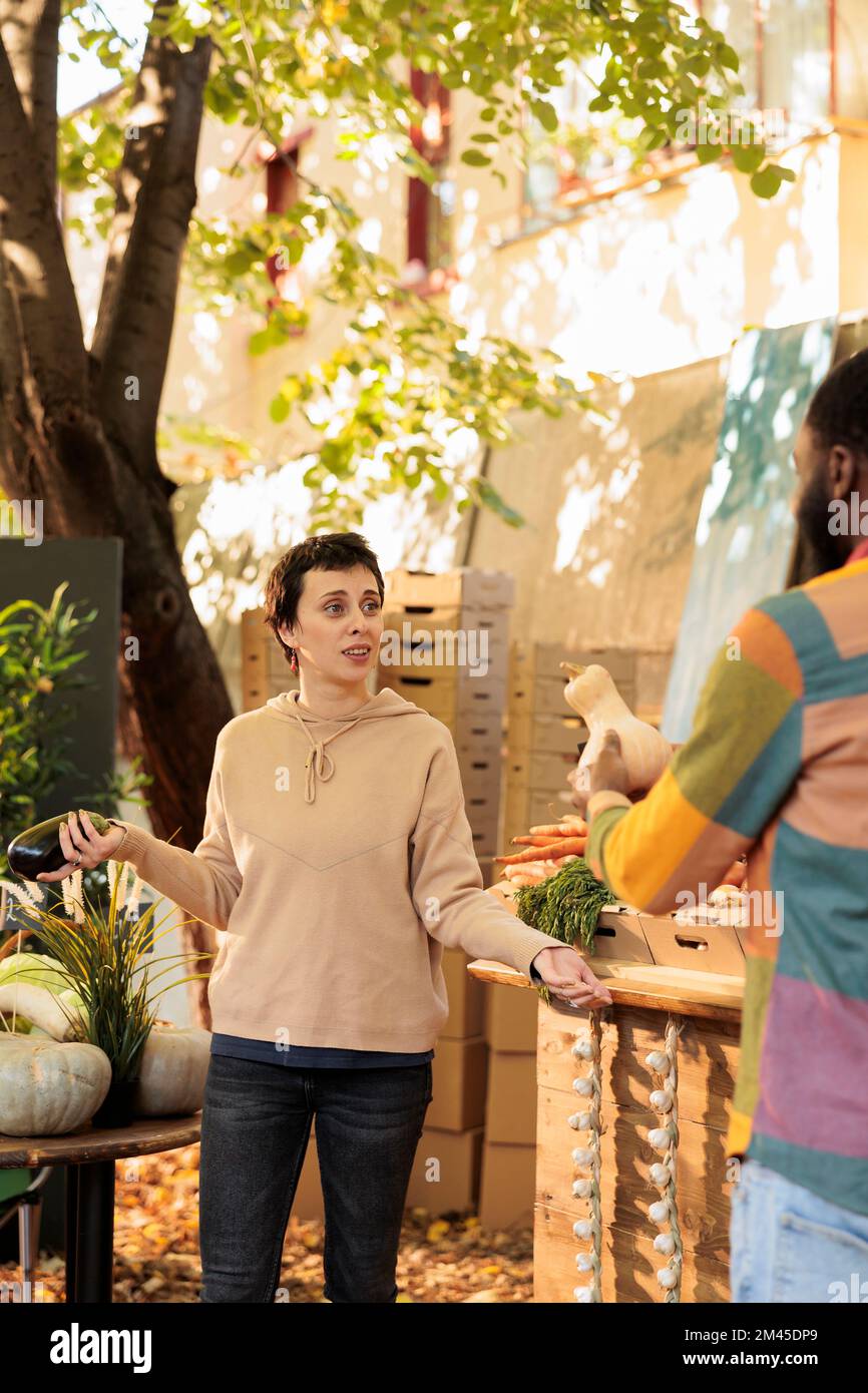 Ein junges, vielfältiges Familienpaar, das sich miteinander unterhält, während es gesundes Bio-Gemüse auf dem Bauernmarkt kauft. Zwei multirassische Freunde, Mann und Frau, die frische lokale Produkte kaufen Stockfoto