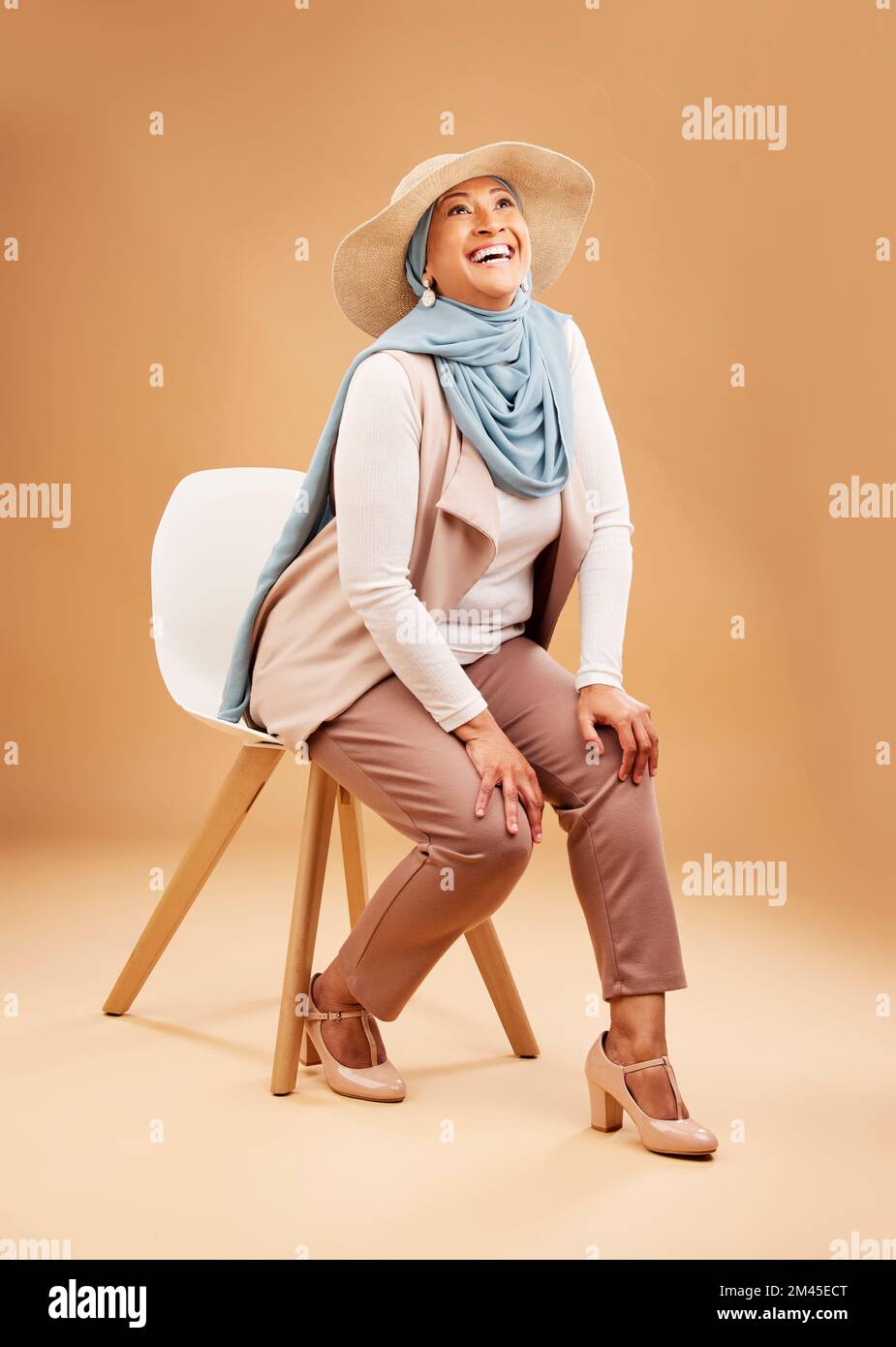 Moslemische Frau, modischer Schal oder Stuhl im Studiohintergrund in stilvollen, trendigen Hüten oder coolen arabischen Kleidern in Dubai. Fröhliches Lächeln, Lachen oder erwachsen Stockfoto