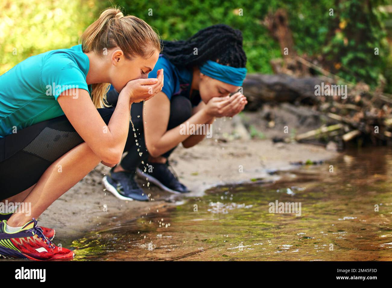 Der Lauf hat uns durstig gemacht. Zwei sportliche junge Frauen, die Wasser aus einem Wasserlauf trinken. Stockfoto Der Lauf hat uns durstig gemacht. Zwei sportliche junge Frauen, die Wasser aus einem Wasserlauf trinken. Stockfoto