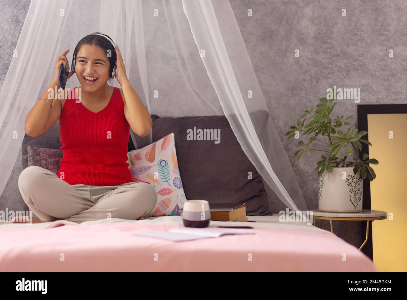 Fröhliches Teenager-Mädchen, das Musik über Kopfhörer hört, während es auf dem Bett sitzt Stockfoto