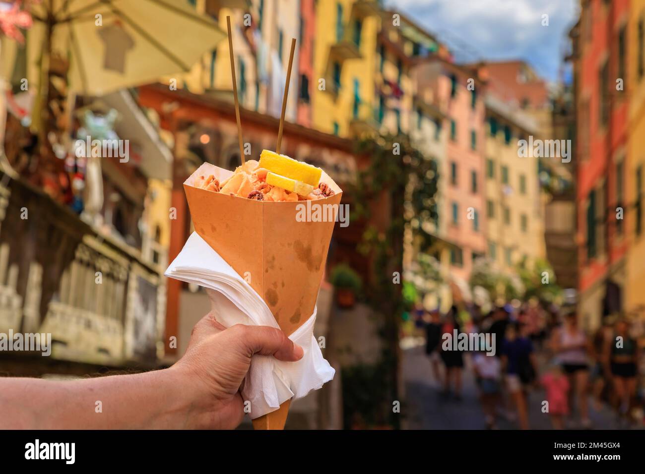 Eine Hand mit einem Konus Fritto misto, einer italienischen Street Food Mischung aus gebratenen Calamari und Garnelen mit bunten Häusern in Riomaggiore, Cinque Terre Italien Stockfoto