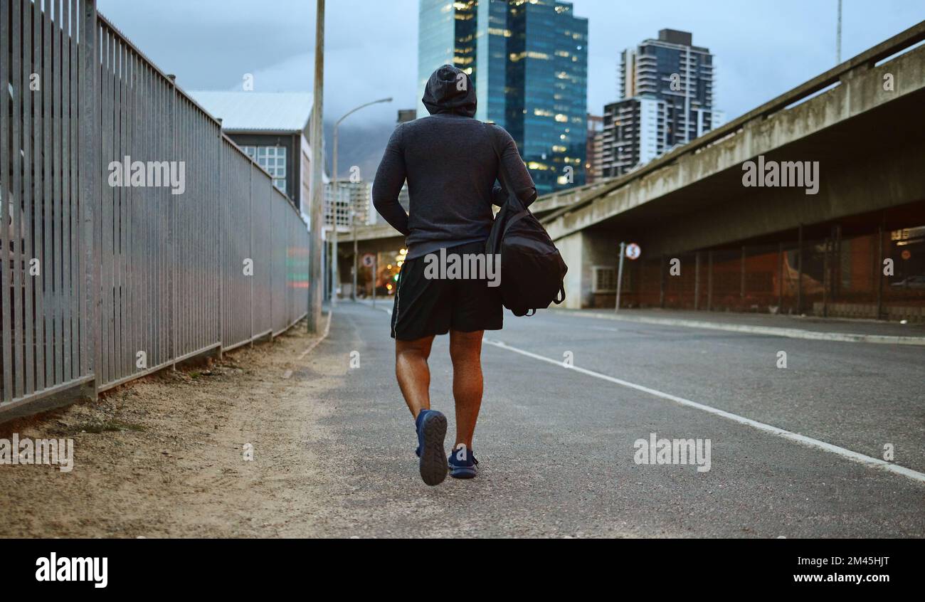 Fitness, schwarzer Mann und Laufen auf der Straße nach dem Laufen, Training und Gym-Workout mit einem Hoodie in der Nacht. Die Rückseite eines männlichen Athleten im städtischen Miami Stockfoto