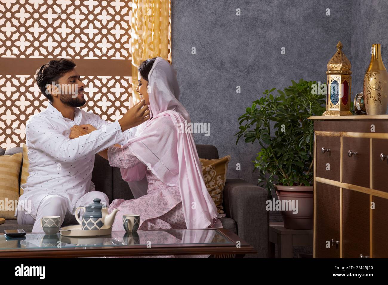 Eine muslimische Frau knöpft das Hemd ihres Mannes und ihr Mann streichelt ihre Wange Stockfoto