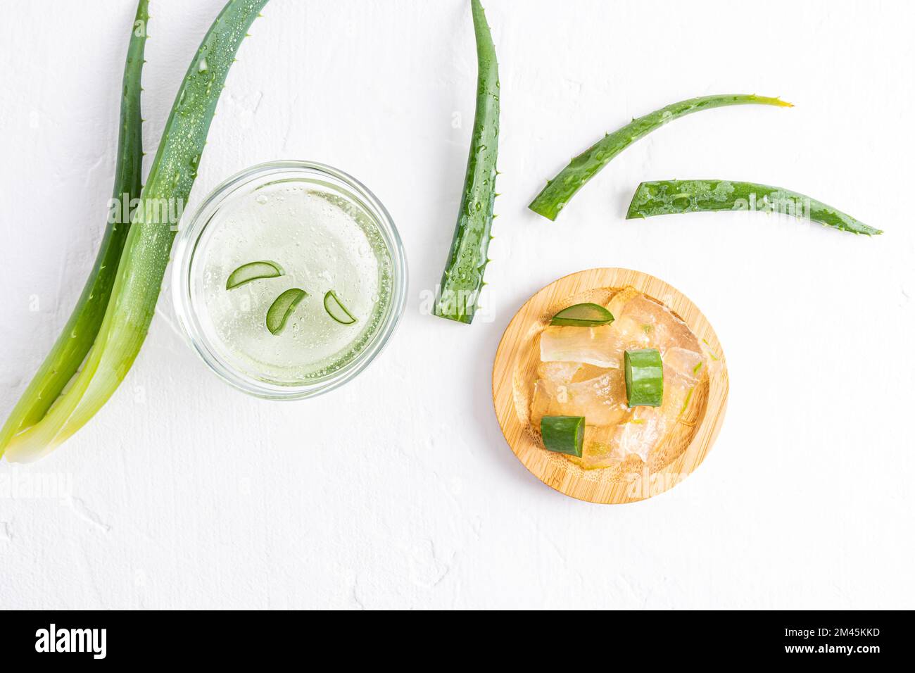 Stücke von durchsichtigem Fruchtfleisch aus Aloe-Vera-Blättern in einer Holzschüssel auf weißem Hintergrund zwischen den saftigen Blättern der Pflanze. Natürliche Hautpflege Stockfoto