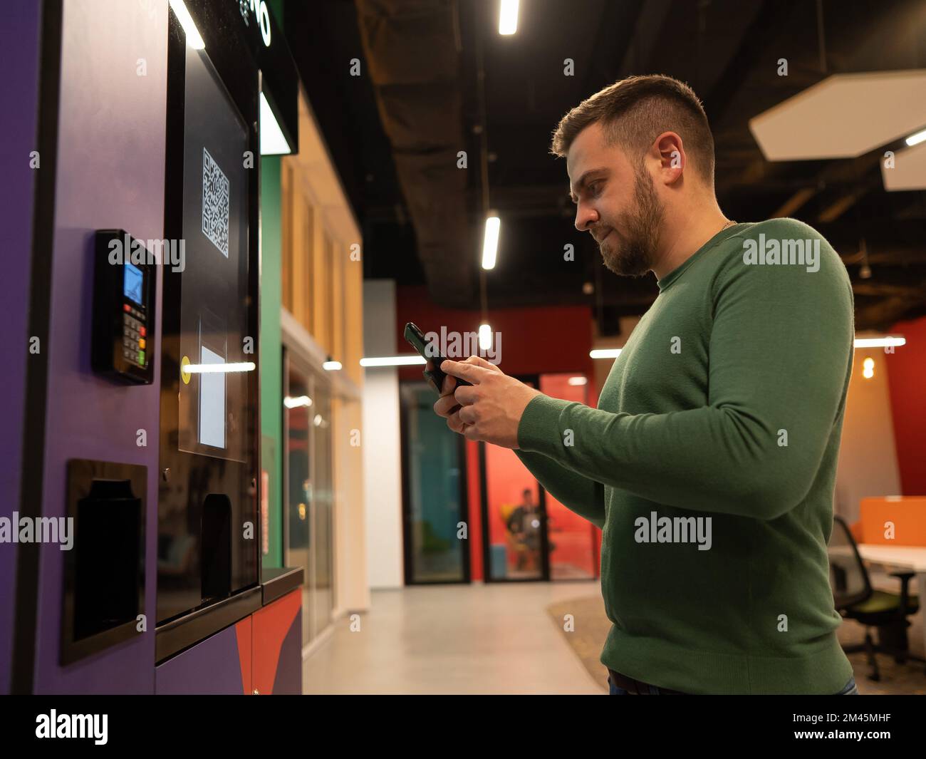 Ein weißer Mann bezahlt per Smartphone für Kaffee in einer Selbstbedienungsmaschine mit qr-Code. Stockfoto