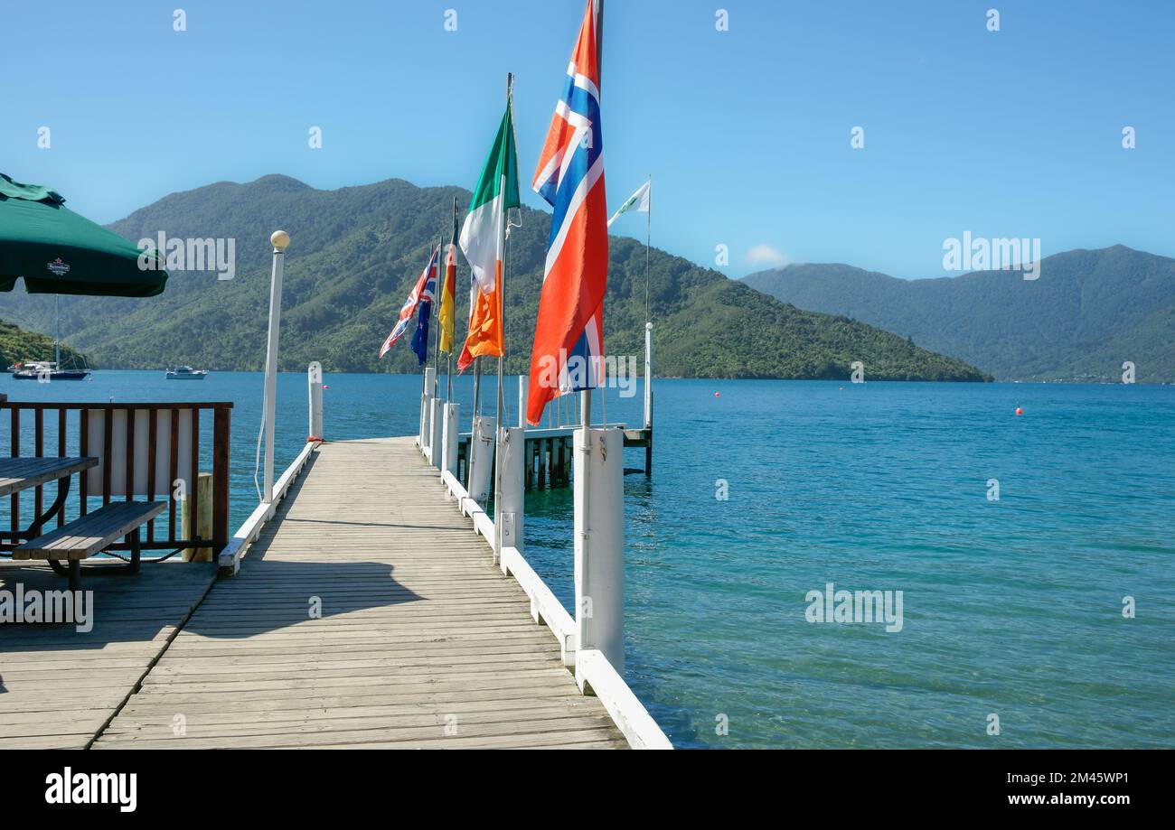 Pier mit Flaggen, die in die malerische Bucht projizieren, umgeben von Buschhügeln mit Marlborough Sounds, Neuseeland. Stockfoto