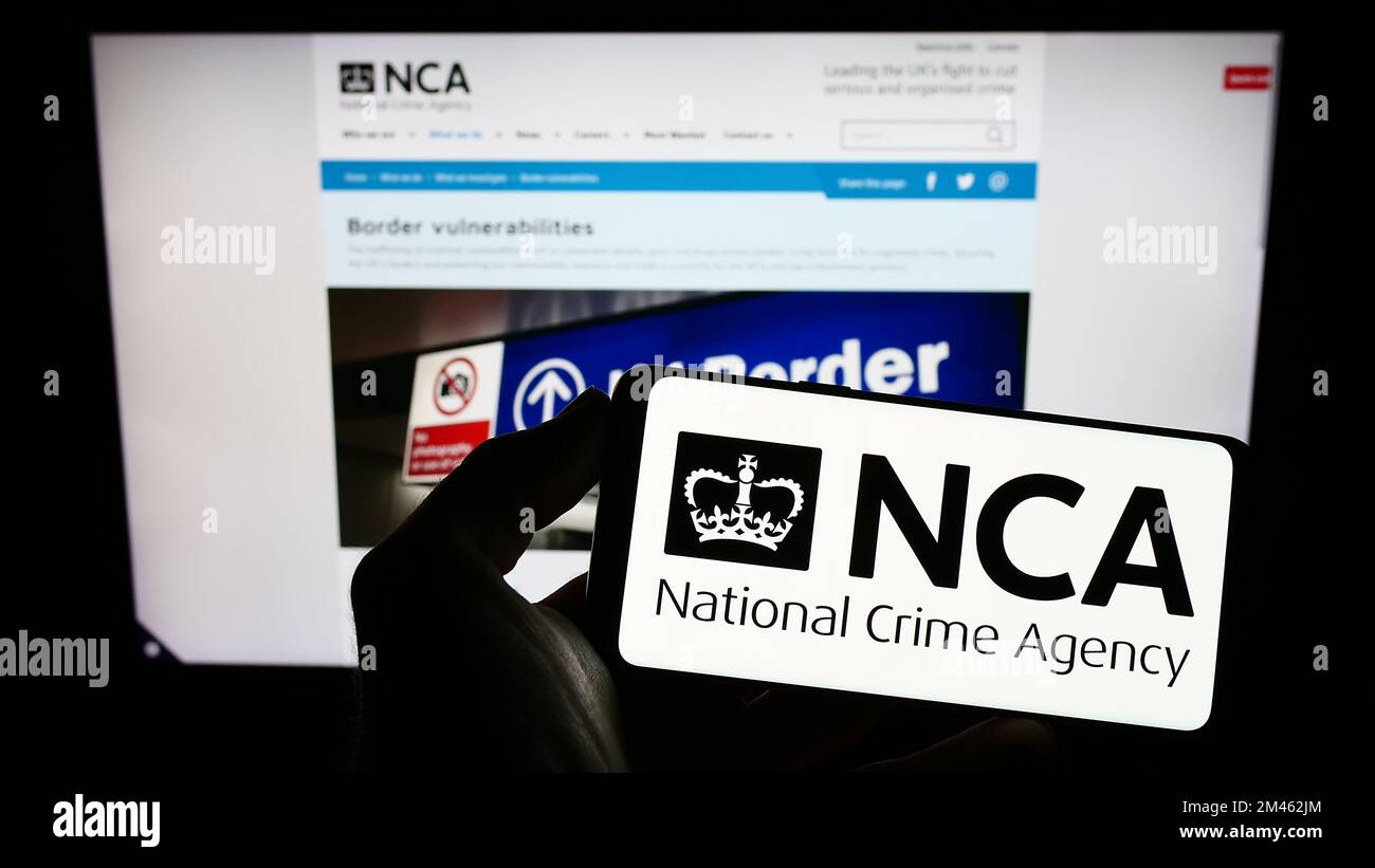 Person, die ein Mobiltelefon mit dem Logo der British National Crime Agency (NCA) auf dem Bildschirm vor der Webseite hält. Konzentrieren Sie sich auf das Display des Telefons. Stockfoto