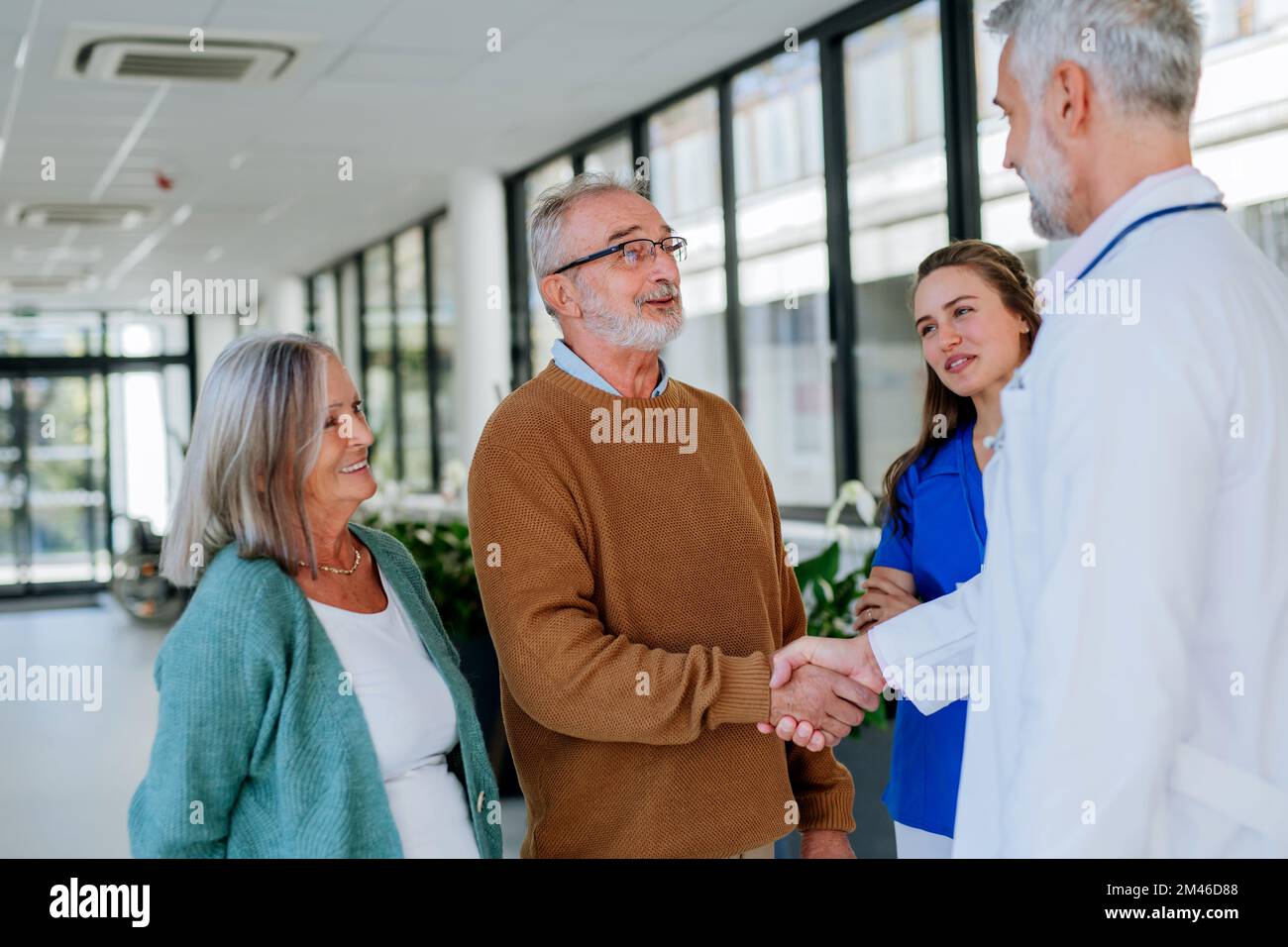 Ein reifer Arzt und sein junger Kollege sprechen mit seinen älteren Patienten auf dem Krankenhausflur. Stockfoto