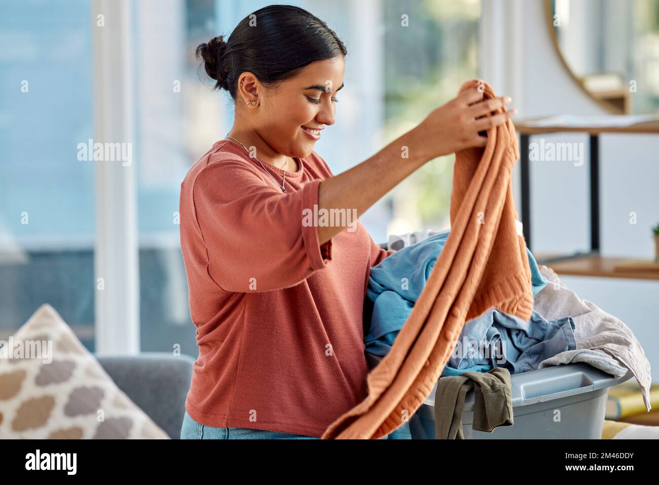 Reinigung, Wäschekorb und Frau mit Kleidung zu Hause, die sich zum Waschen der Kleidung fertig macht. Frühjahrsputz, Hygiene und glückliche Frau, die sich auf Stoff vorbereitet Stockfoto