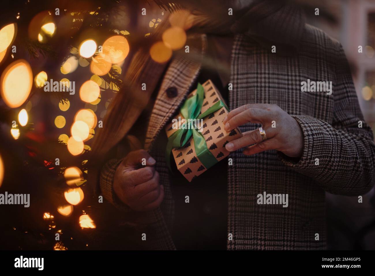 Nahaufnahme eines Mannes, der ein kleines Geschenk in seiner Tasche versteckt, draußen auf dem Weihnachtsmarkt. Stockfoto