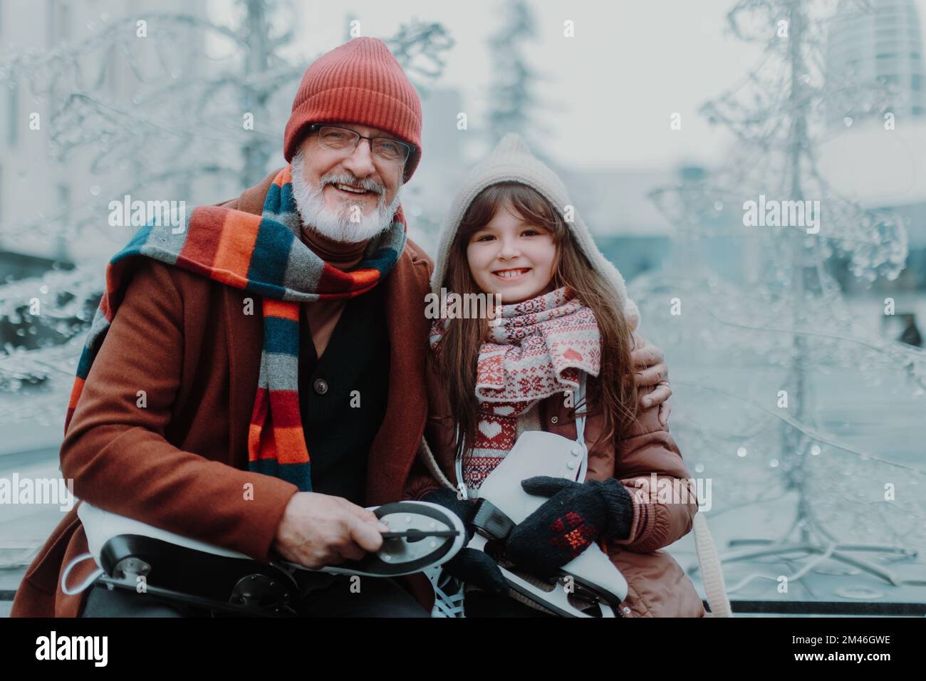 Porträt von Großvater und Enkeltochter im Winter auf der Eislaufbahn im