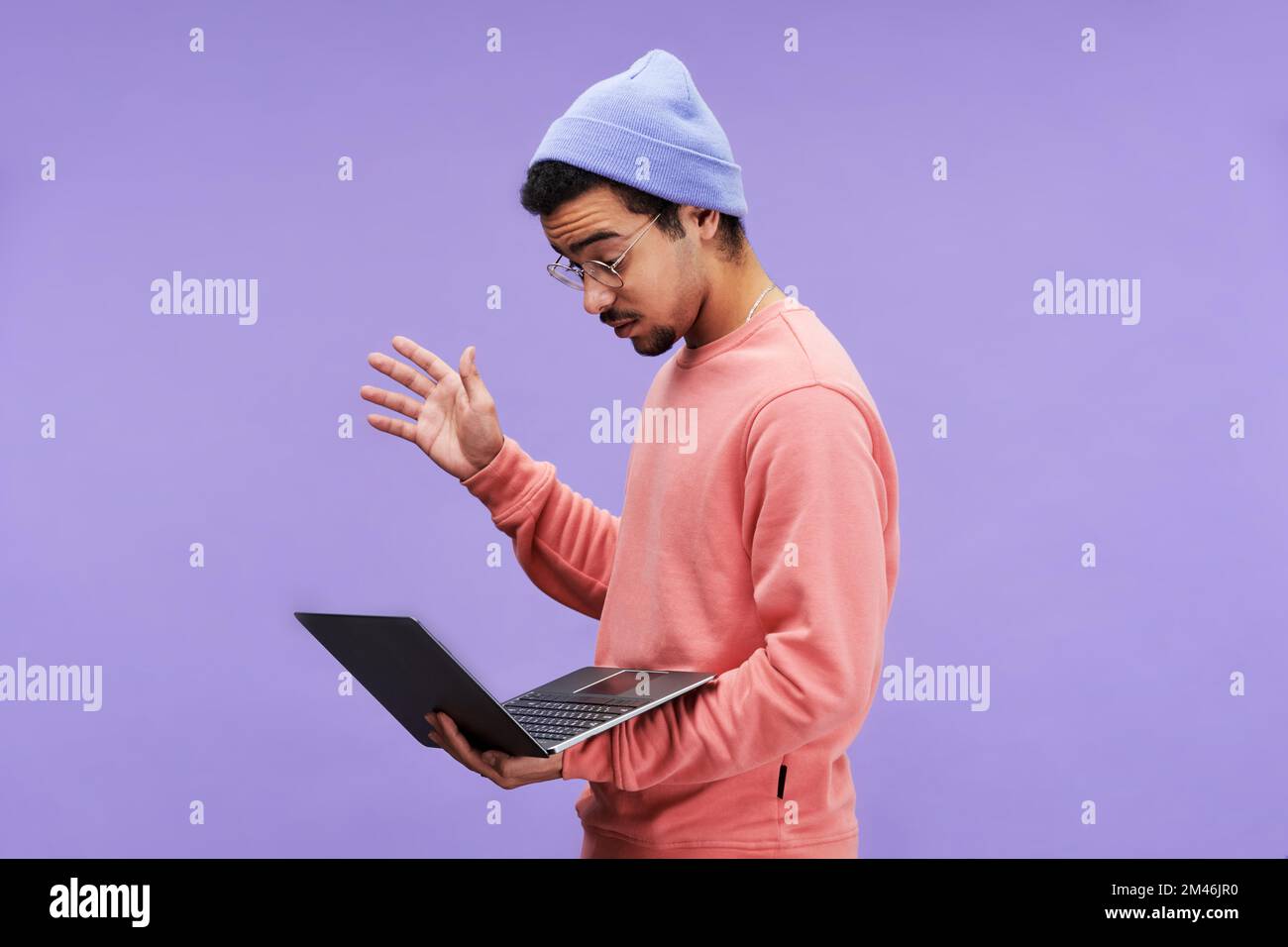 Seitenansicht eines jungen, erstaunten männlichen Programmierers in Freizeitkleidung und Brille, der auf den Laptop-Bildschirm blickt, während er mit einem technischen Problem konfrontiert ist Stockfoto