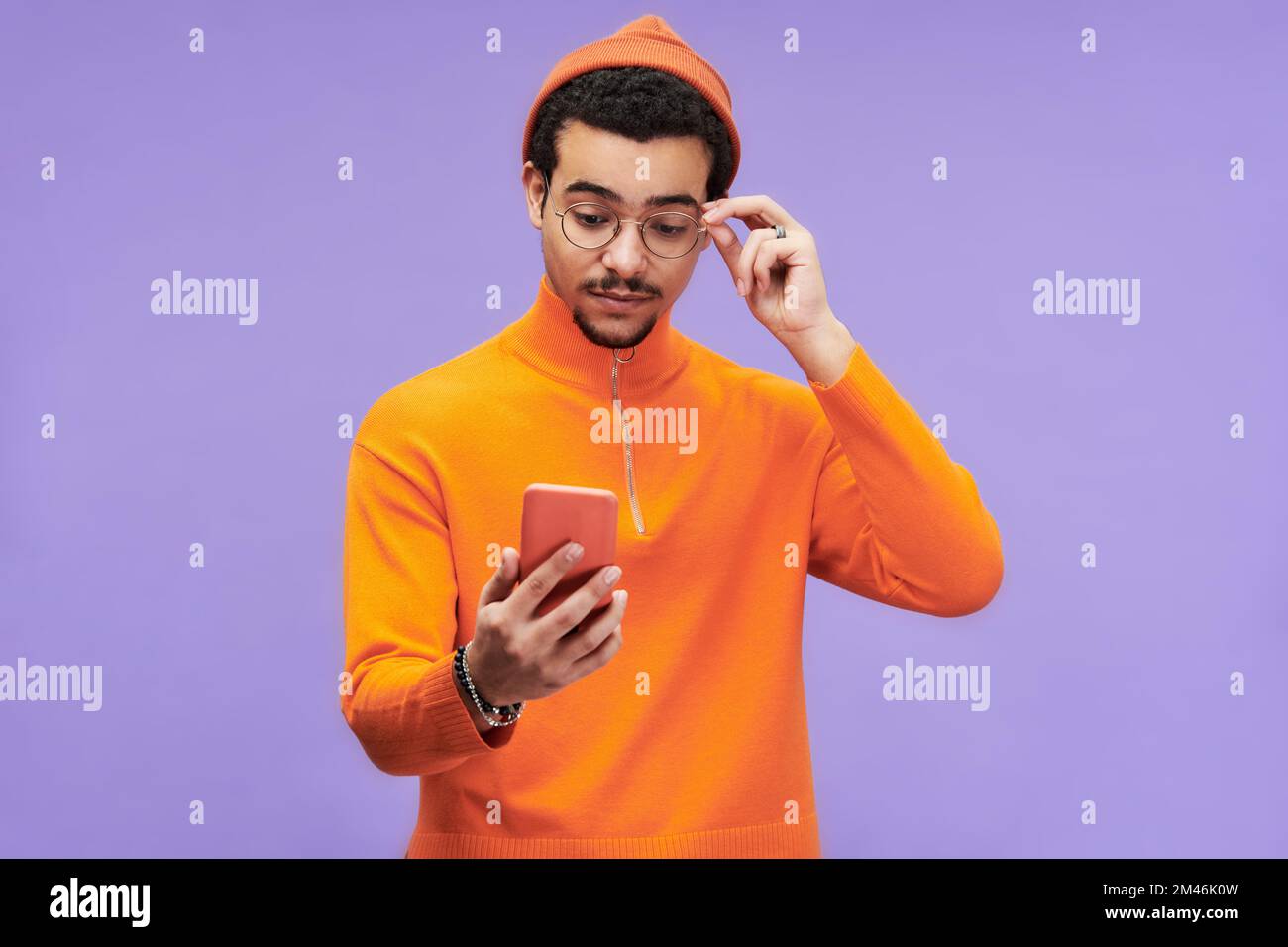 Junger Mann, der Missverständnisse ausdrückt, während er eine Brille berührt und mit Werbung oder Verkaufsankündigung auf den Smartphone-Bildschirm schaut Stockfoto