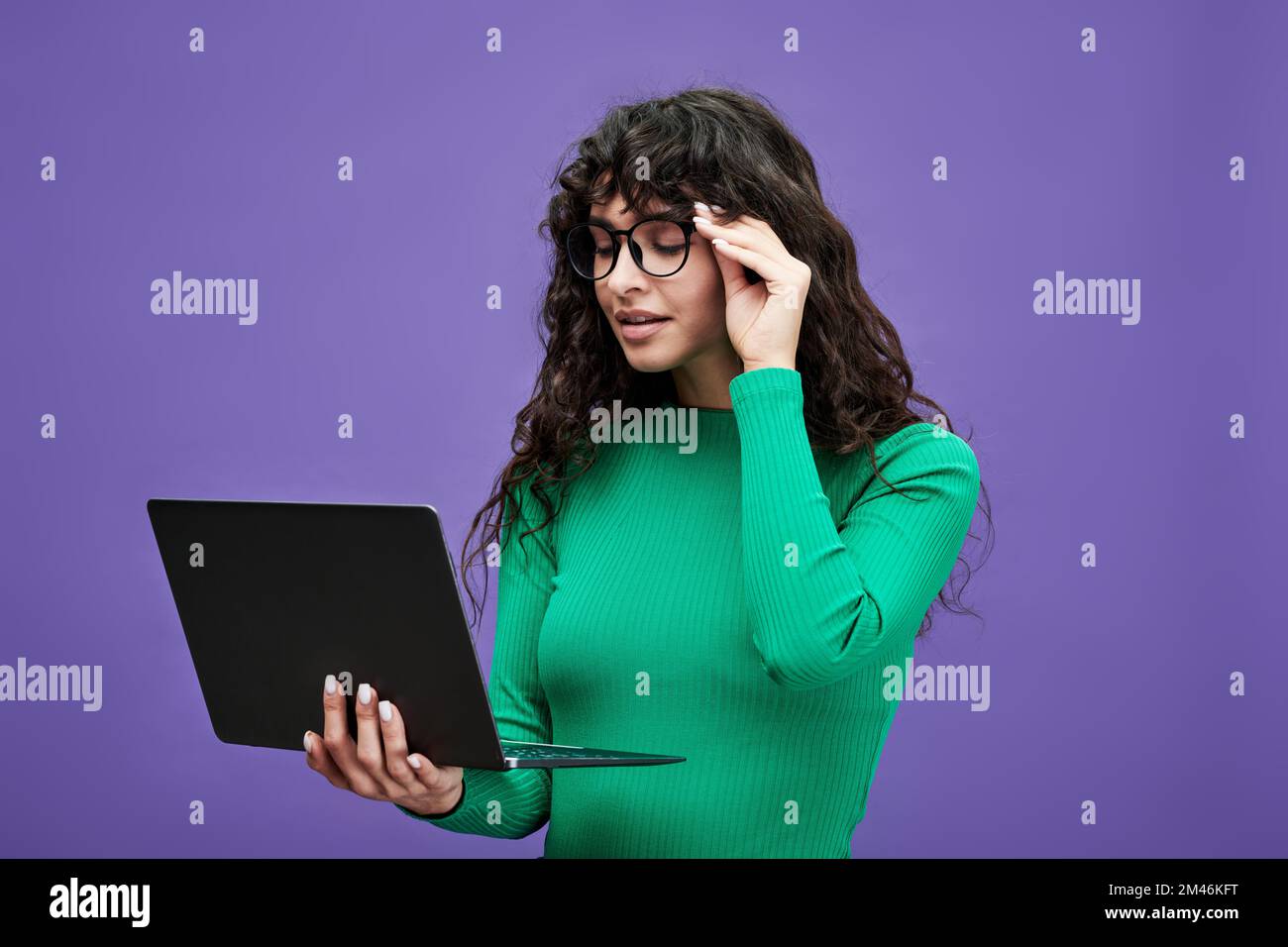Junge Geschäftsfrau oder Lehrerin in einem grünen Pullover und einer Brille, die auf den Laptop-Bildschirm schaut, während sie sich Online-Informationen ansieht Stockfoto