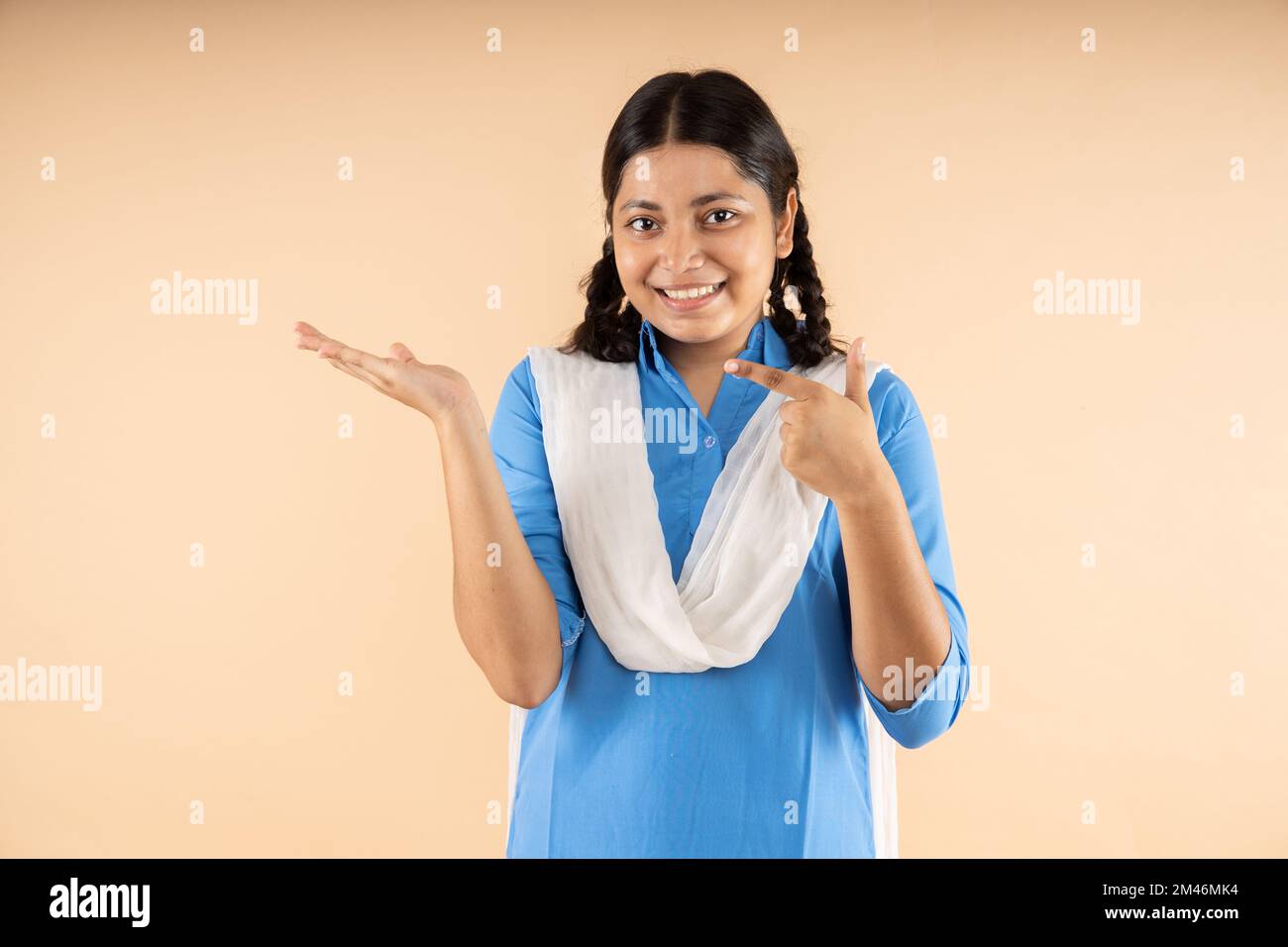 Glückliches indisches Studentenmädchen in blauer Schuluniform, die auf leere Flächen zeigt, um Werbung oder Beförderung isoliert über B zu platzieren Stockfoto