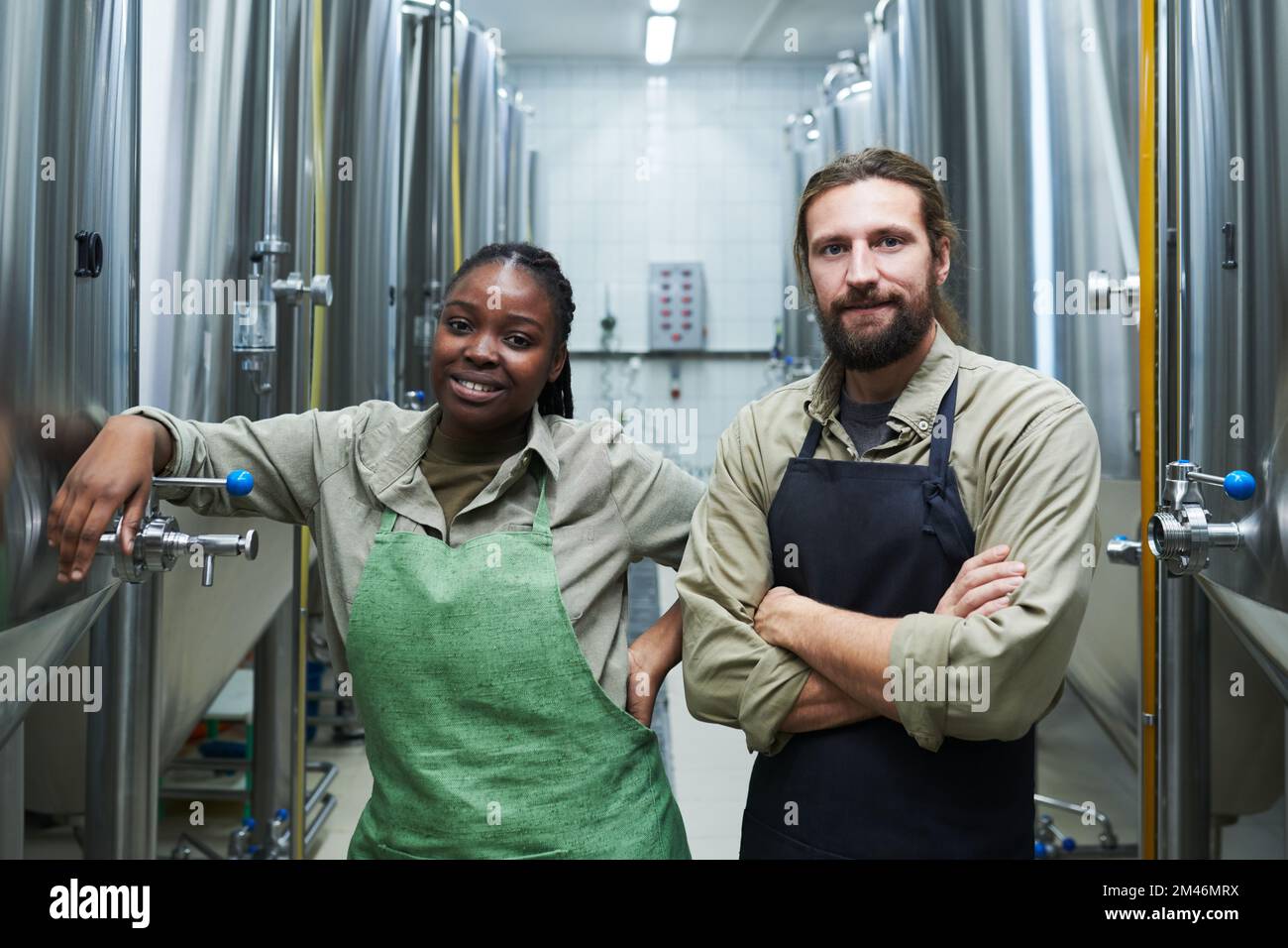 Positives, vielfältiges Team von Mikrobrauereiarbeitern, die unter den Geräten für die Gärung stehen Stockfoto