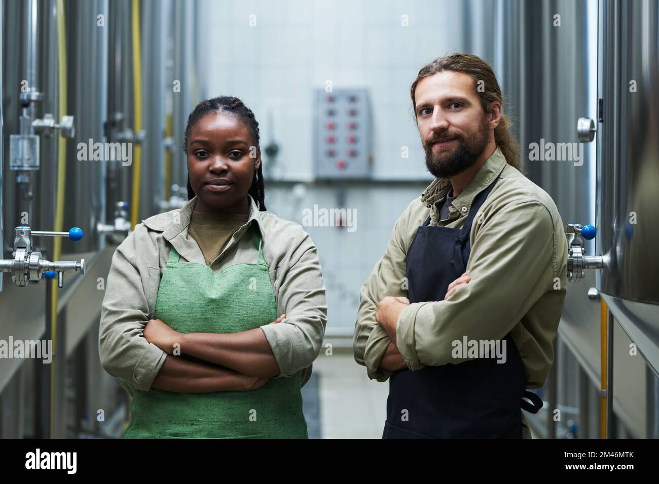 Ein lächelndes Team aus Mikrobrauereiarbeitern, die mit verschränkten Armen stehen Stockfoto