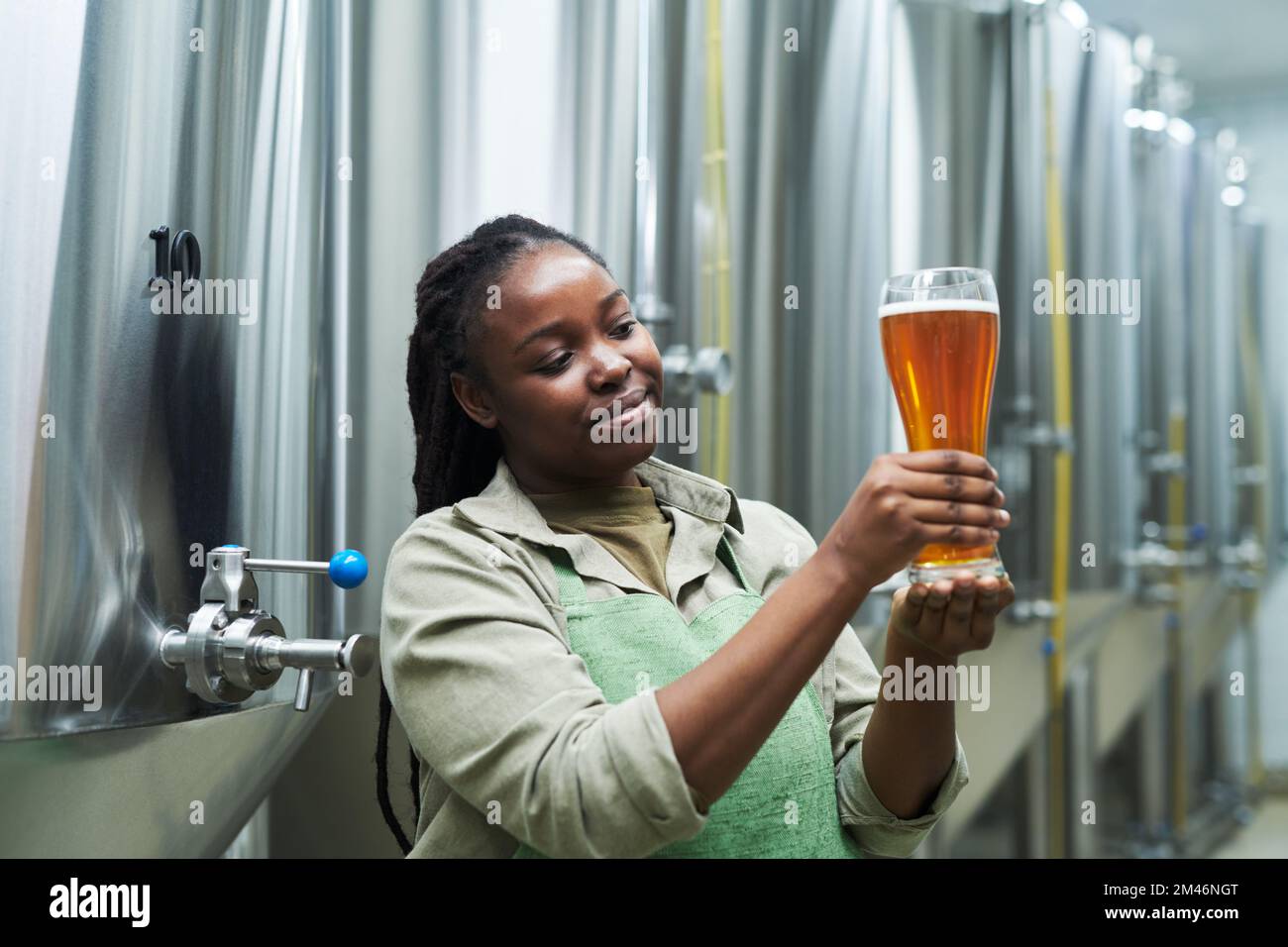 Fröhliche Frau, die Bier aus ihrer kleinen Brauerei zeigt Stockfoto