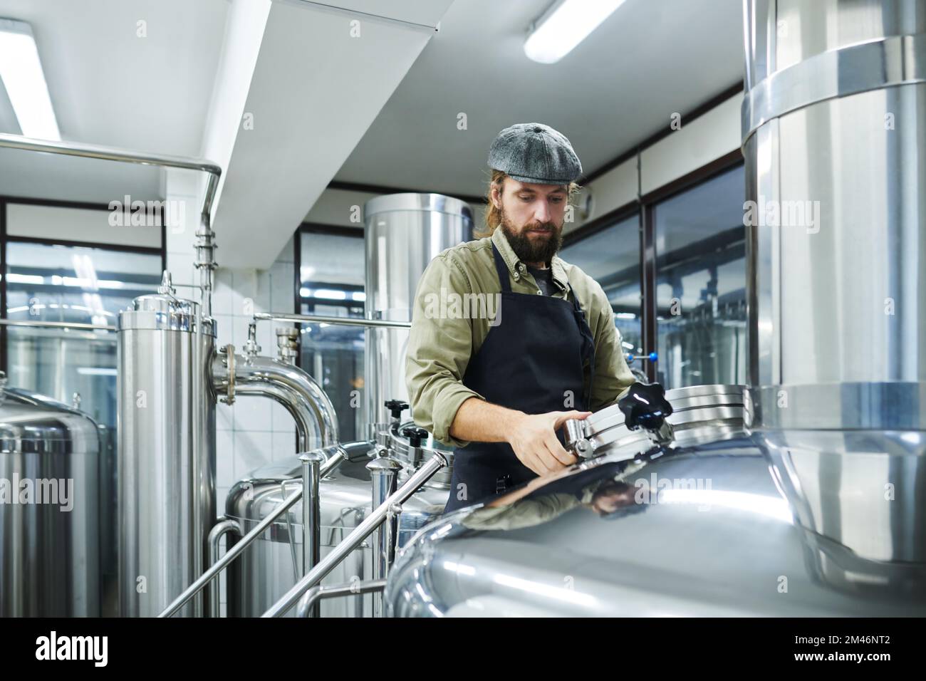 Kleiner Brauereiarbeiter, der Tanks mit fermentierendem Bier überprüft Stockfoto