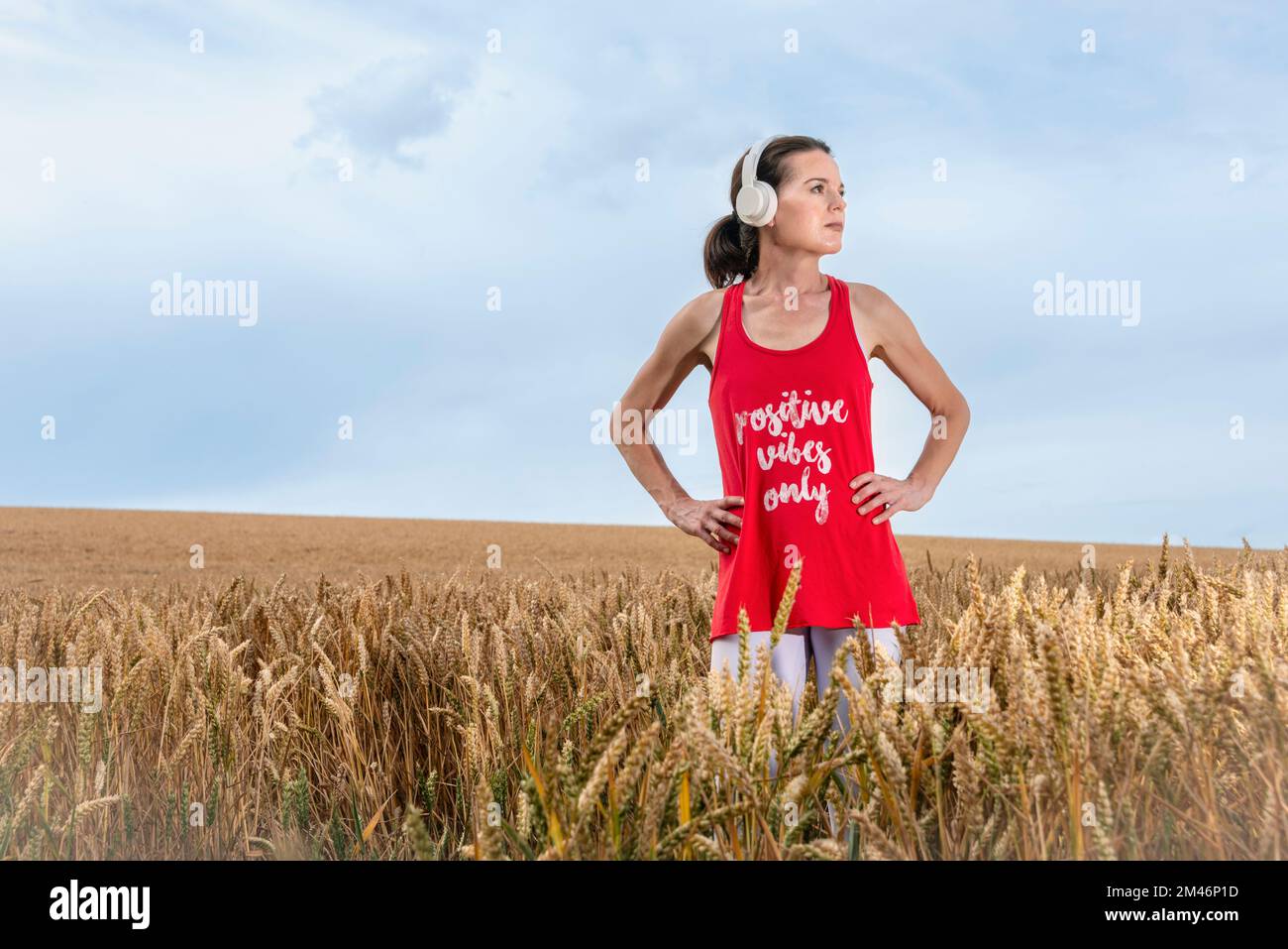 Frau, die auf einem Feld steht und Musik auf Kopfhörern hört, positive Vibes nur T-Shirt. Stockfoto