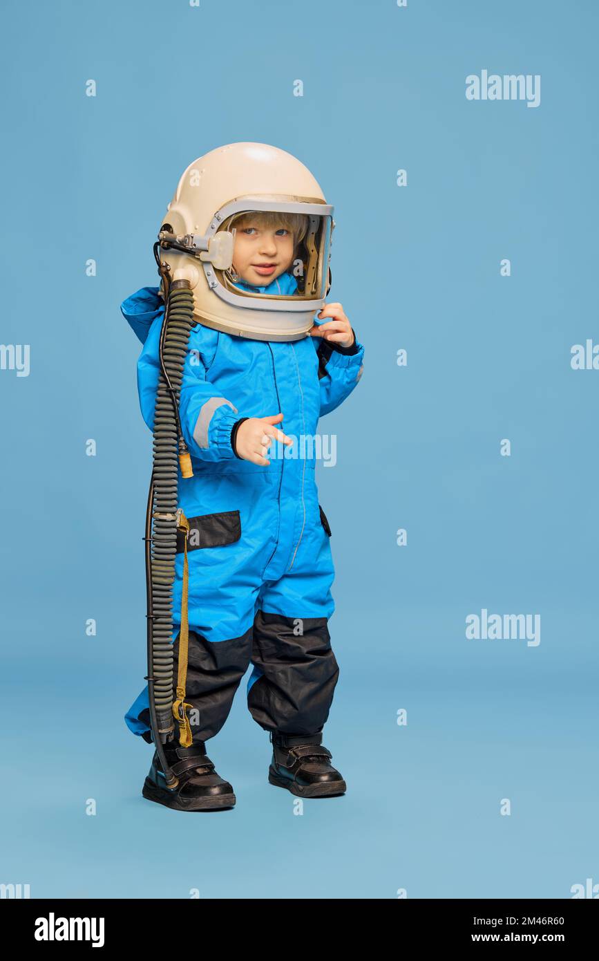 Porträt eines kleinen Jungen, Kind, das im Astronautenkostüm posiert, mit blauem Studiohintergrund. Fantastisches Spiel, Träume. Kindheitsbegriff, Emotionen Stockfoto