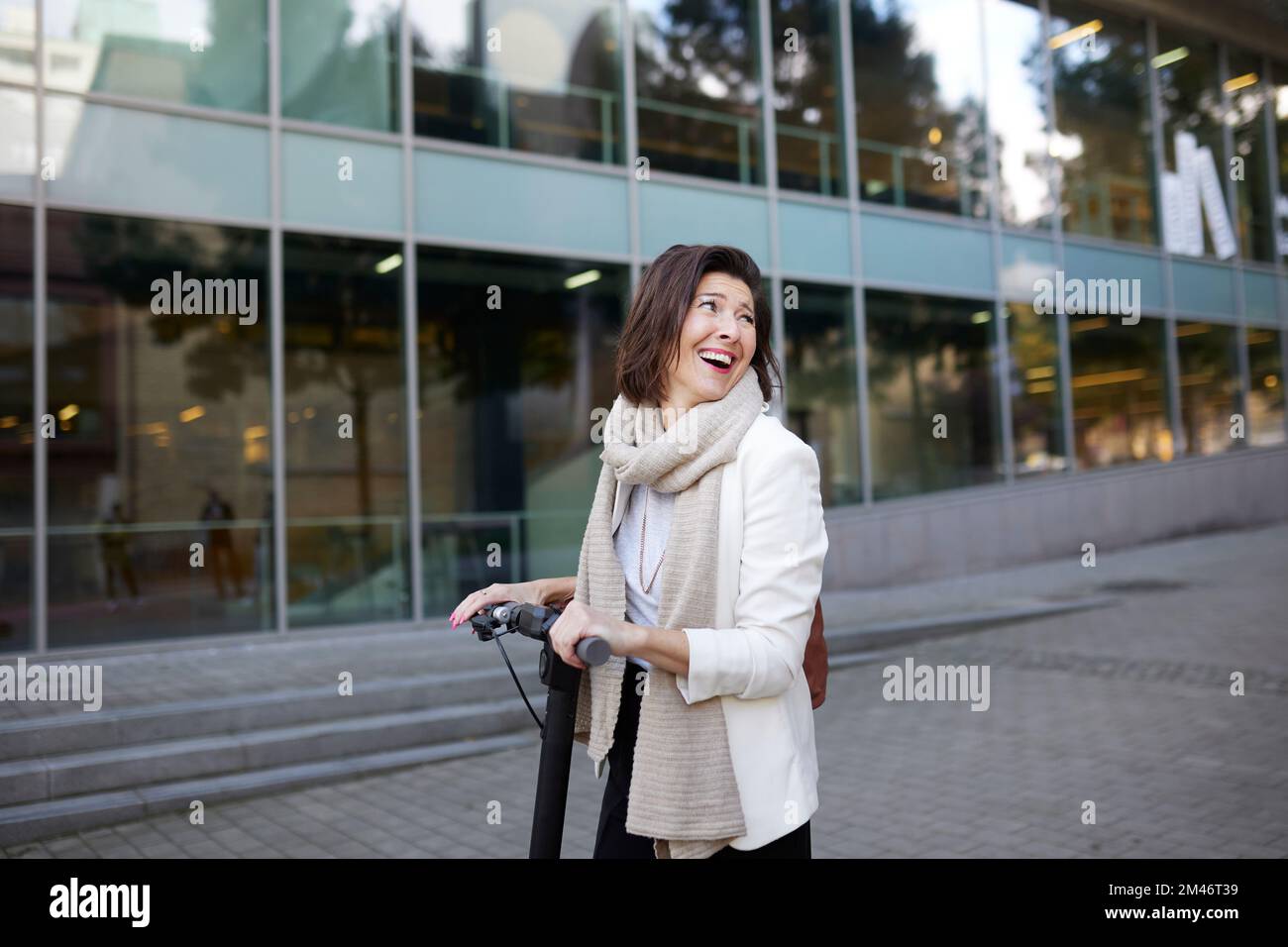 Lächelnde Geschäftsfrau mit elektrischem Roller Stockfoto