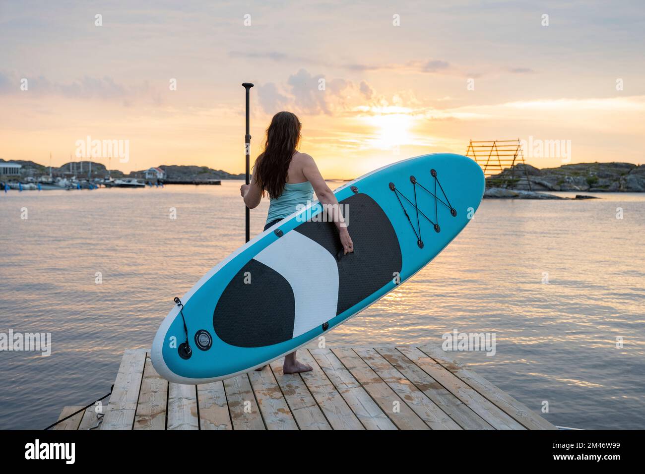 Eine Frau trägt ein Paddleboard auf dem Steg Stockfoto