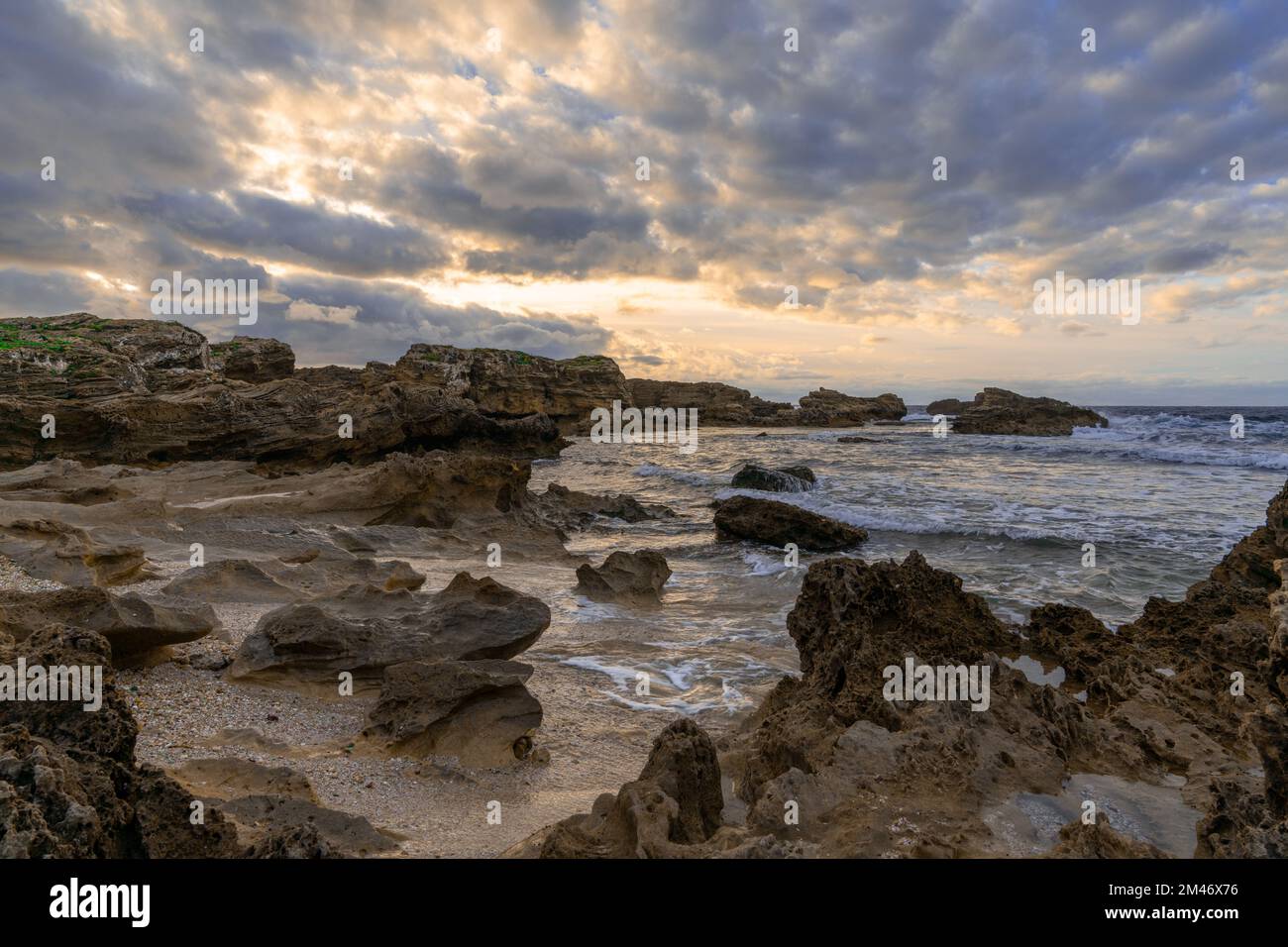 Eine felsige Bucht und ein Sandstrand unter einem ausdrucksstarken Sonnenuntergangshimmel an der zerklüfteten Westküste Sardiniens Stockfoto