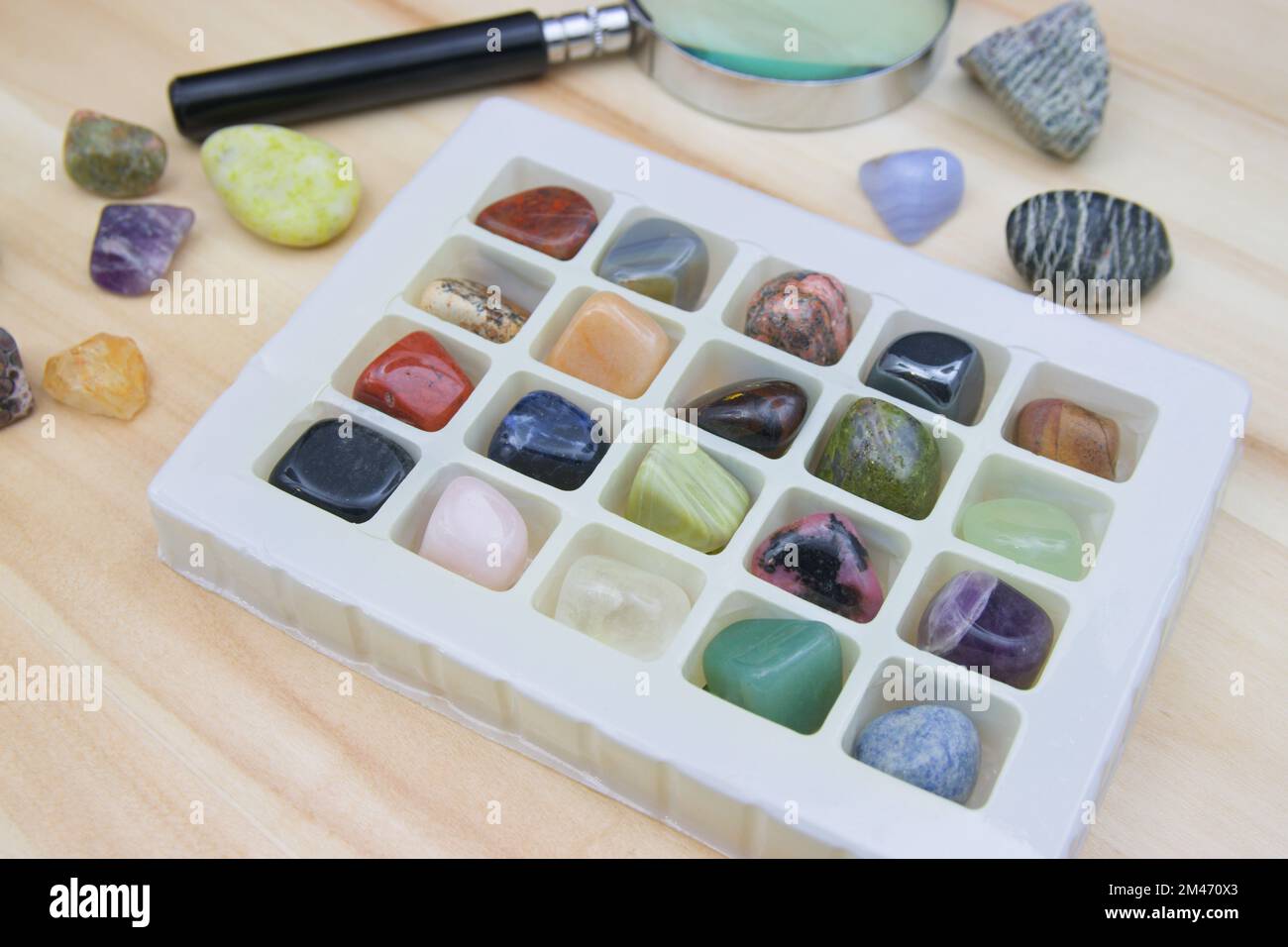 Gruppe von Halbedelsteinen und Mineralien in einem Set, das durch Amateurmineralogie zusammen mit einer Lupe untersucht wird Stockfoto