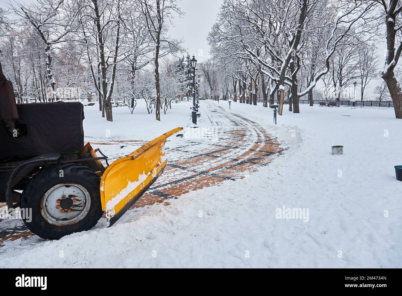 Der Schneeräumtraktor reinigt die Gasse im Park. Traktor entfernt Schnee, streut Salz und Sand, um ein Abrutschen zu verhindern. Kommunale Reinigung von Bürgersteig Stockfoto