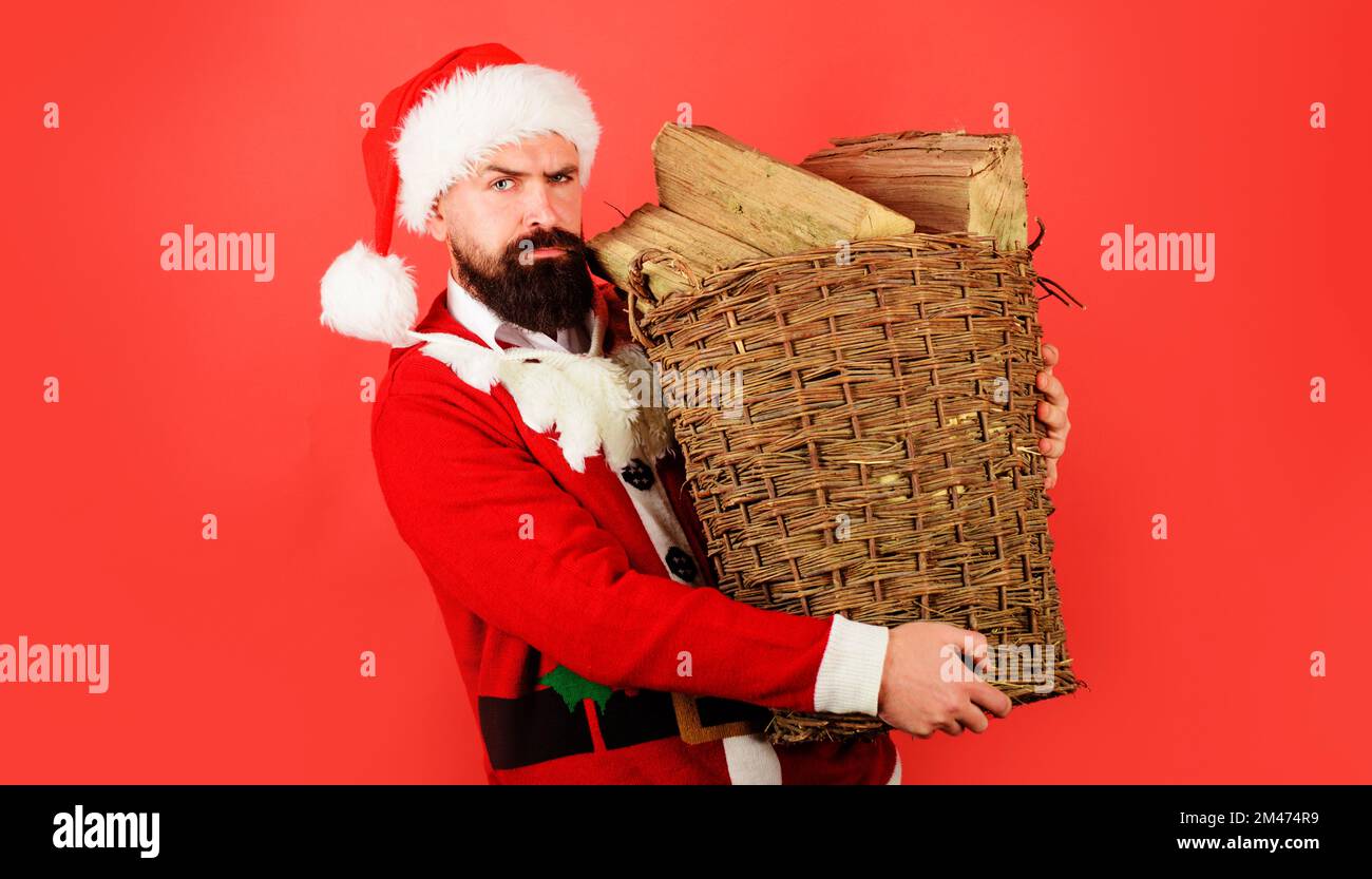 Frohe Weihnachten und Frohes neues Jahr. Ein bärtiger Mann im Weihnachtsmann-Kostüm trägt einen Korb mit Feuerholz. Stockfoto